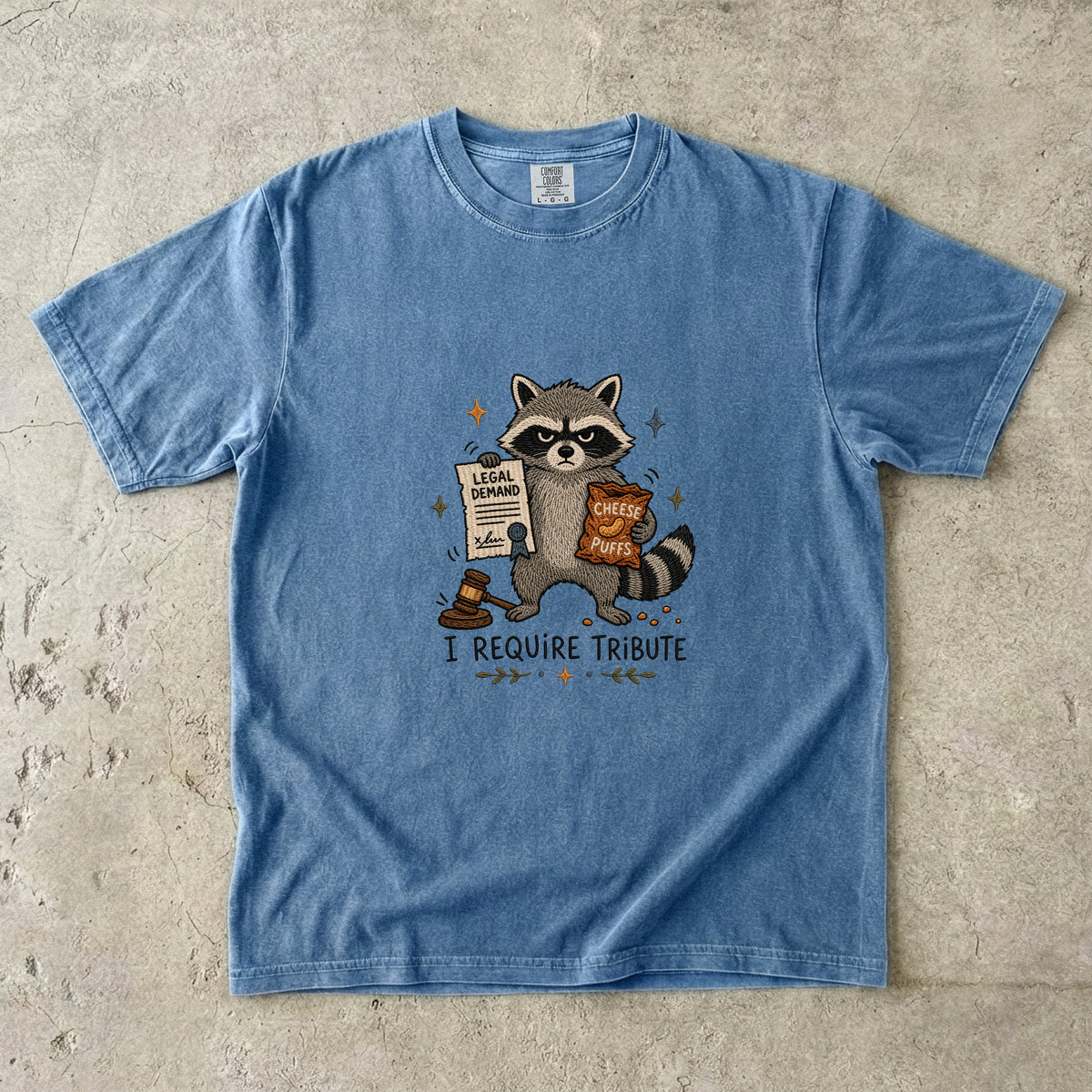 Blue t-shirt with raccoon holding legal demand and cheese puffs, saying "I require tribute."