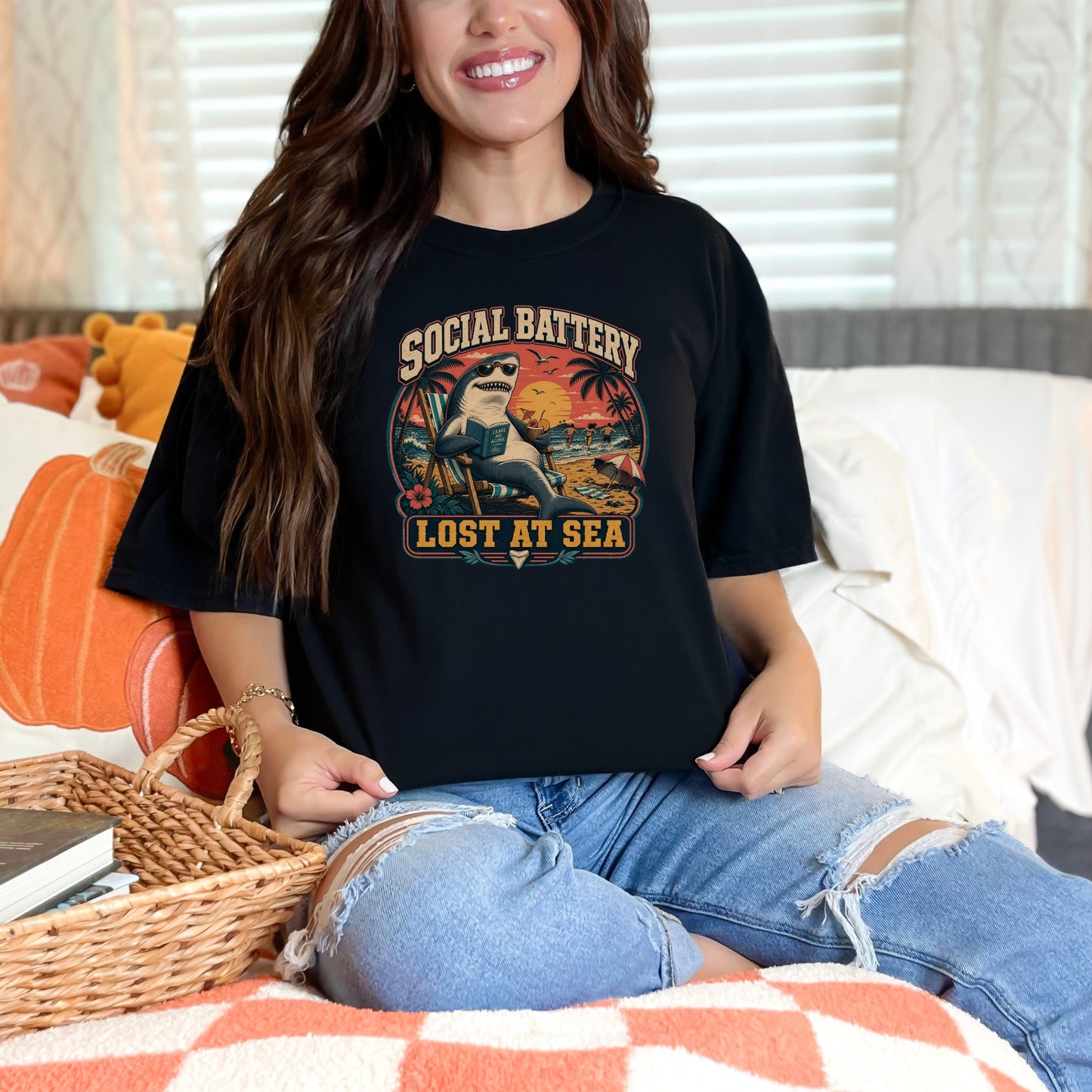 Black t-shirt with a graphic of a shark lounging on a beach chair, reading a book.