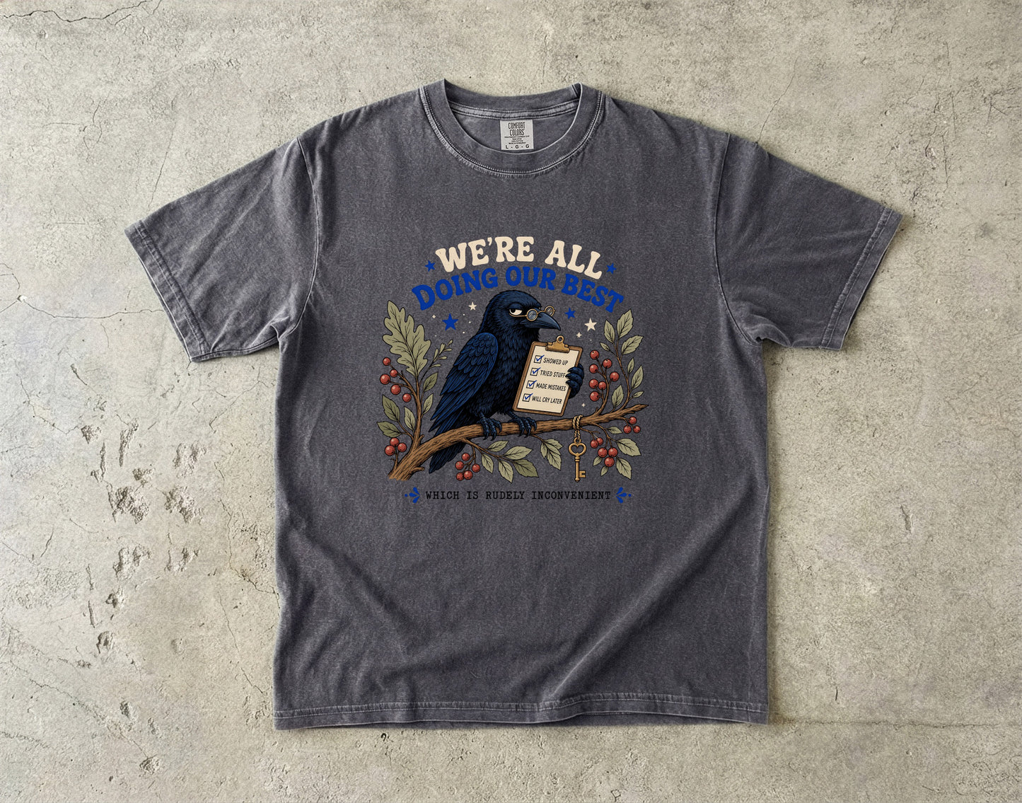T-shirt with a crow on a branch holding a checklist and text saying "WE'RE ALL DOING OUR BEST WHICH IS RUDELY INCONVENIENT".
