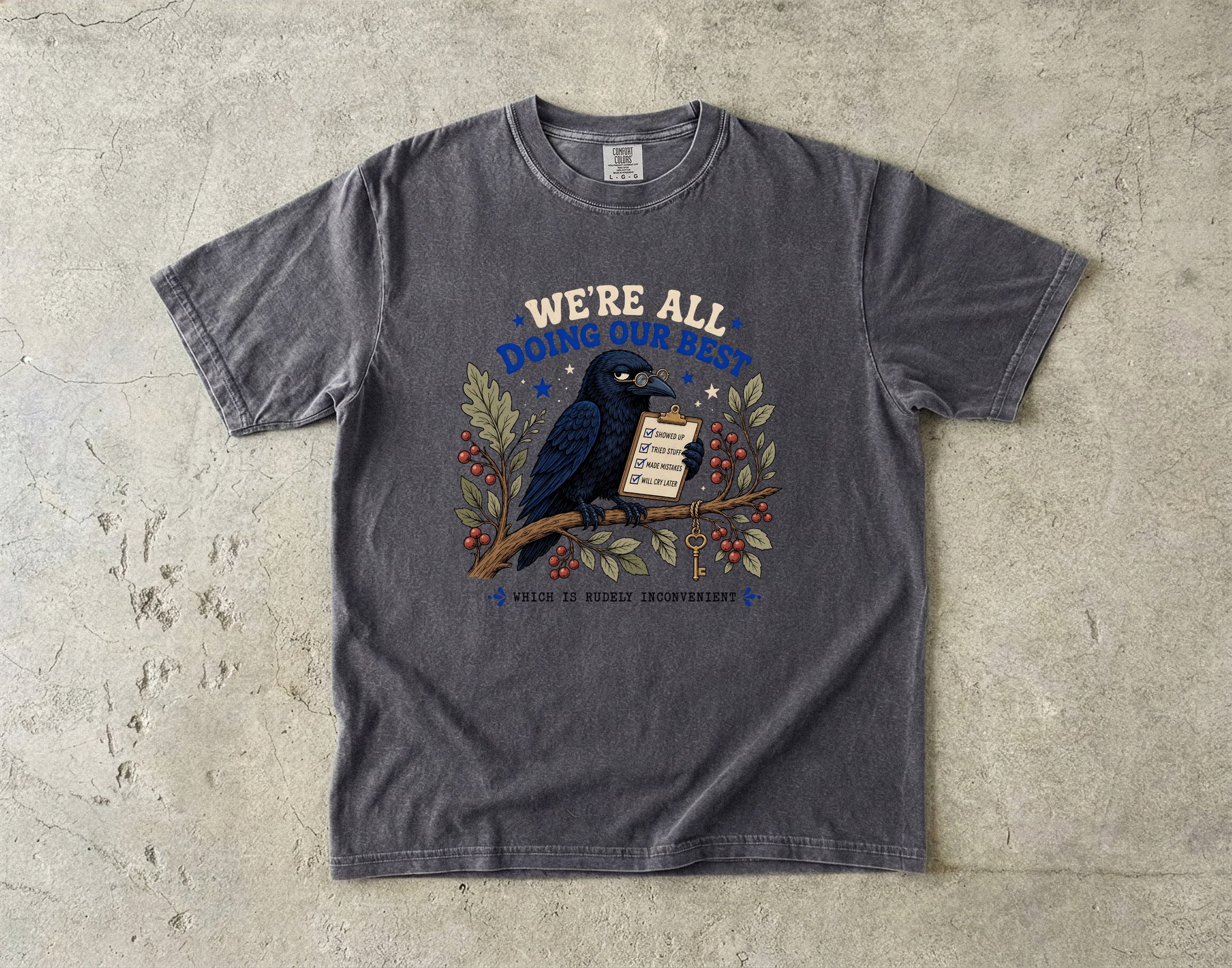 T-shirt with a crow on a branch holding a checklist and text saying "WE'RE ALL DOING OUR BEST WHICH IS RUDELY INCONVENIENT".