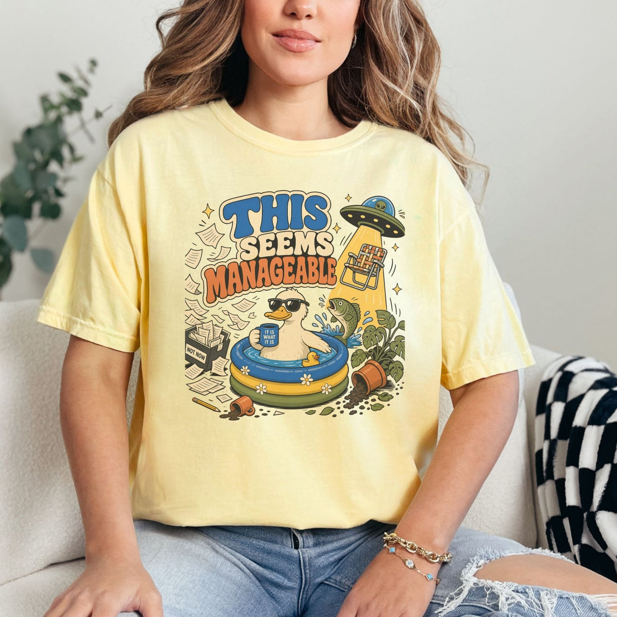 Shirt graphic: duck in a pool, text "THIS SEEMS MANAGEABLE" and flying saucer.