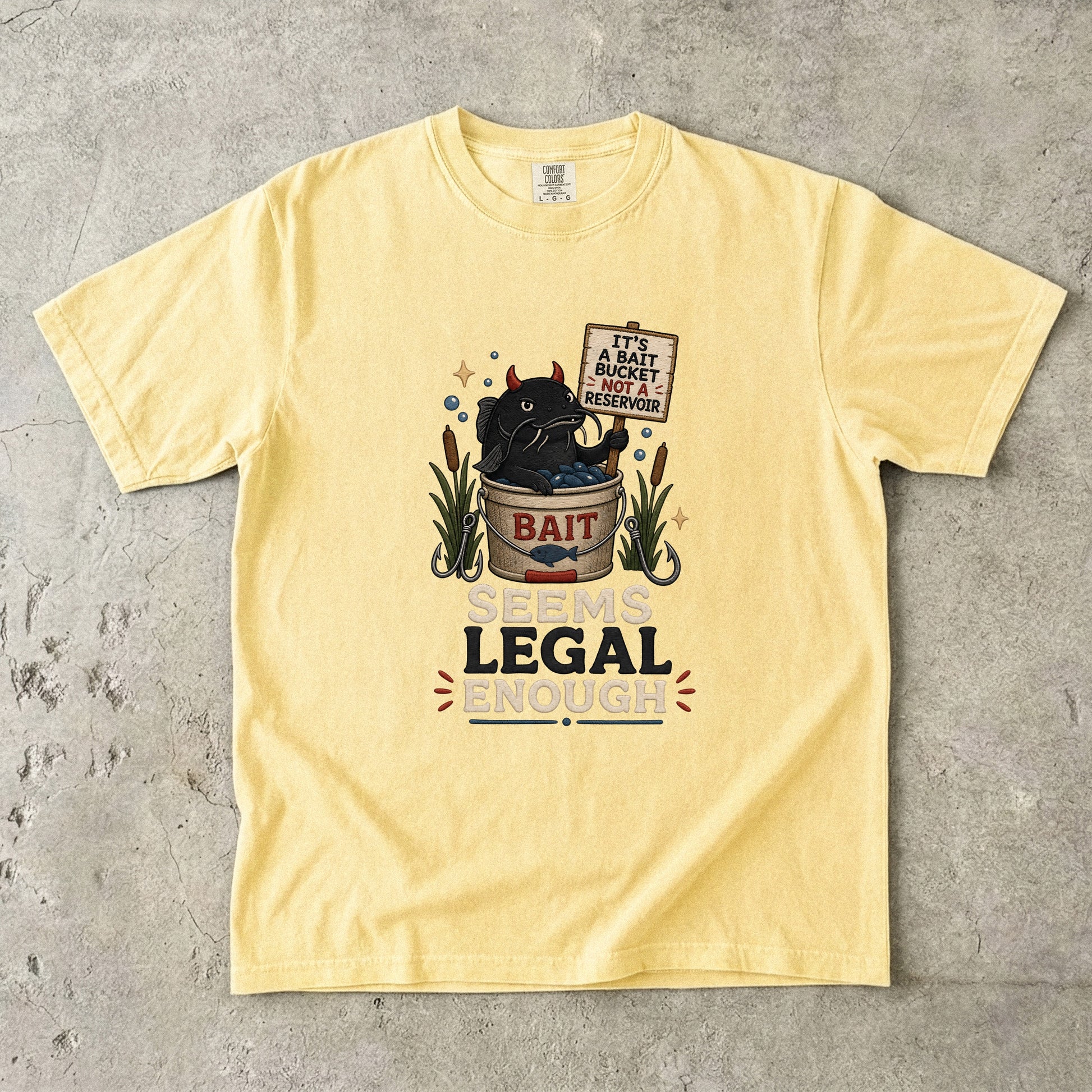 Yellow t-shirt with graphic of devil cat in bait bucket, text reads "It's a bait bucket, not a reservoir" and "Seems Legal Enough".