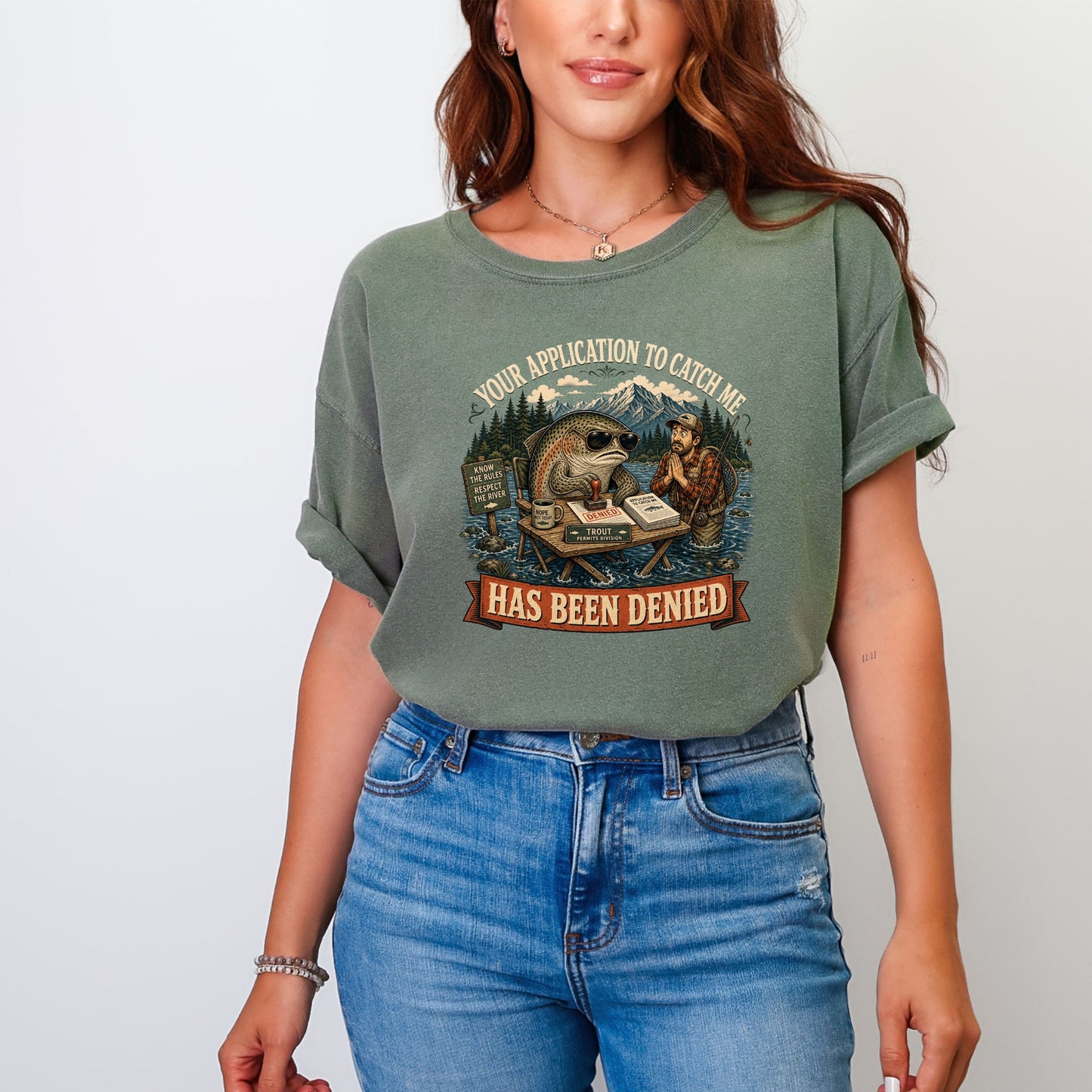 A woman wearing a faded green t-shirt with a humorous graphic showing a fish denying a fisherman's permit application.