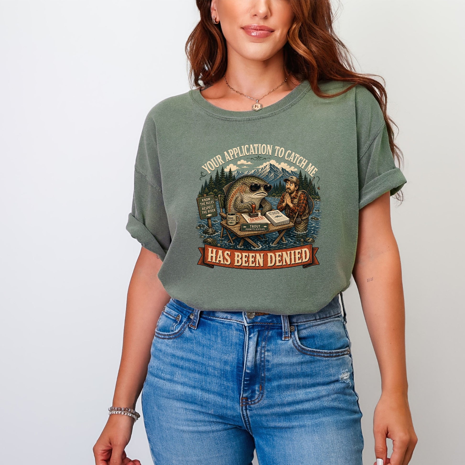 A woman wearing a faded green t-shirt with a humorous graphic showing a fish denying a fisherman's permit application.