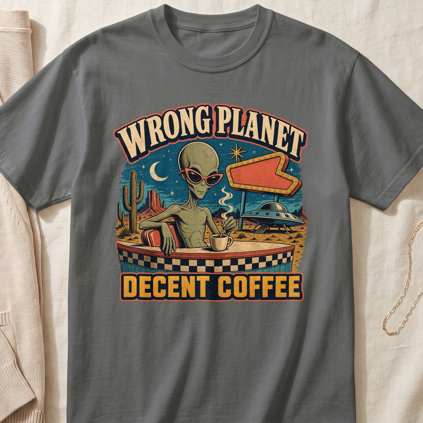 Alien wearing sunglasses sits at a checkered table, drinking coffee with text "Wrong Planet Decent Coffee".