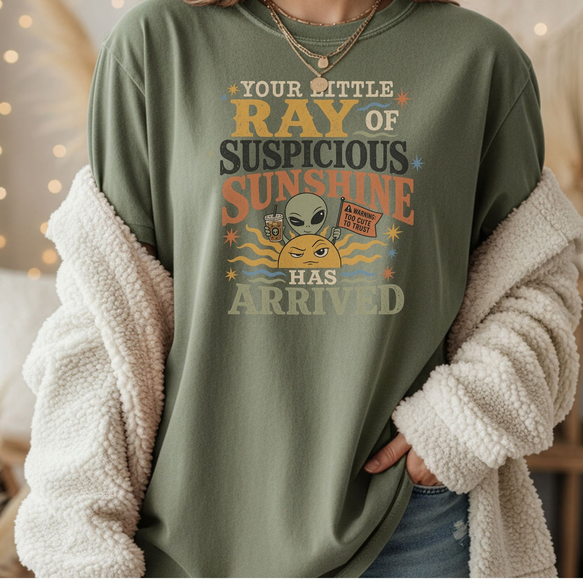 Green t-shirt with graphic "Your little ray of suspicious sunshine has arrived" featuring an alien and sun.