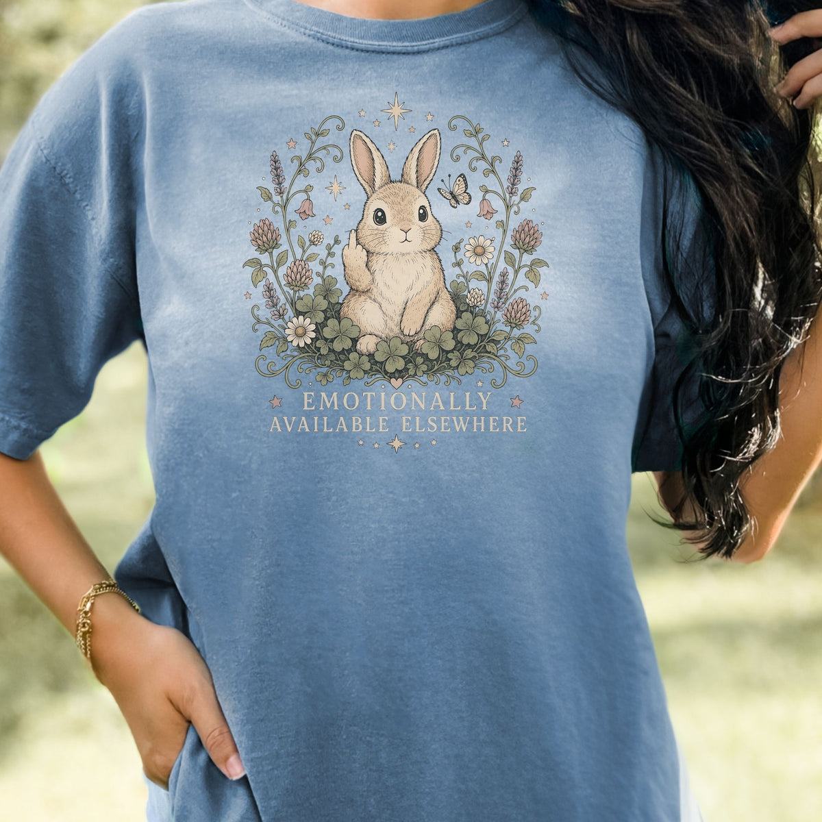 Blue t-shirt with a graphic of a bunny giving the middle finger and text "Emotionally Available Elsewhere."
