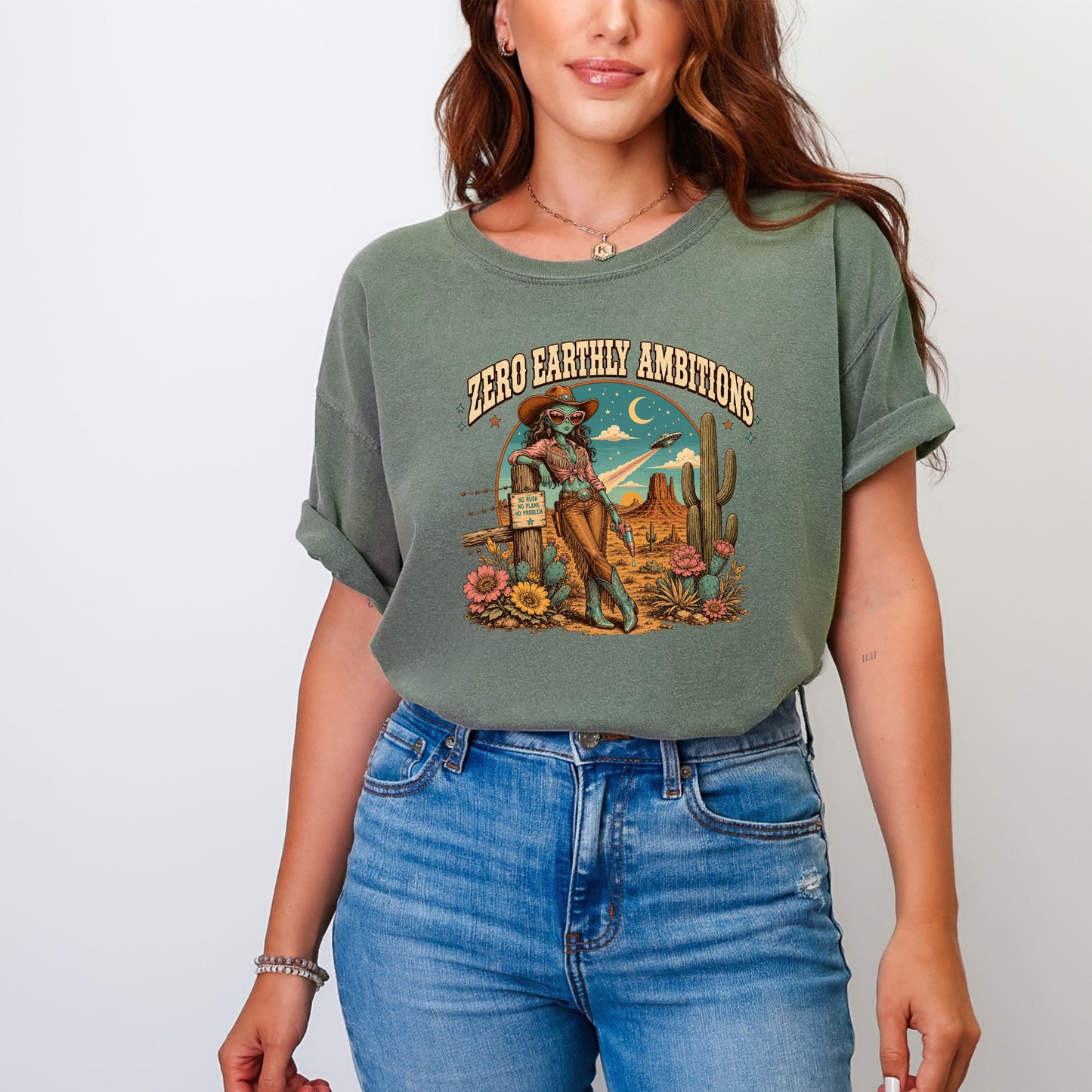 Graphic tee with desert scene, alien cowgirl, and "Zero Earthly Ambitions" text.