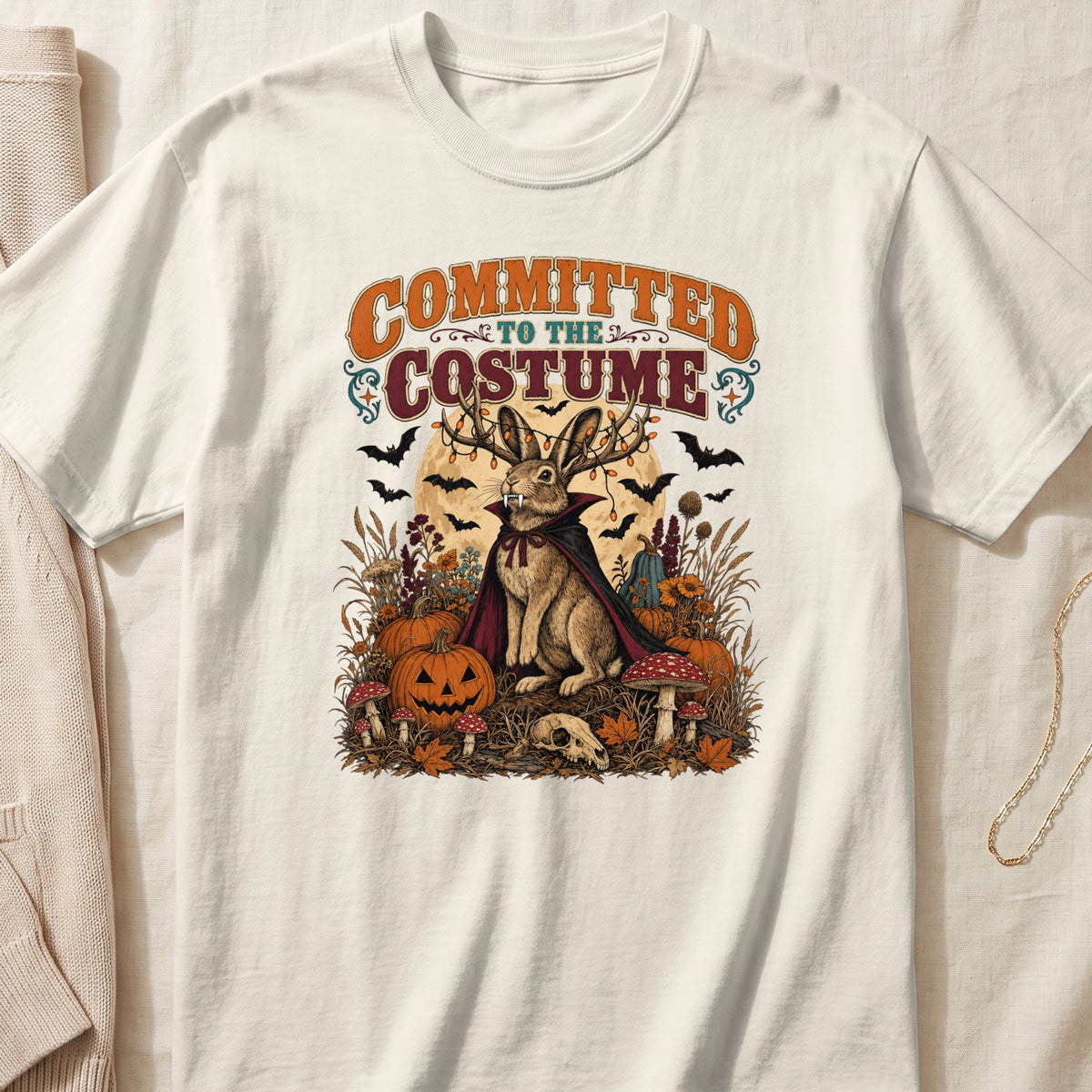 Rabbit in a cape with antlers and vampire fangs surrounded by Halloween decorations.