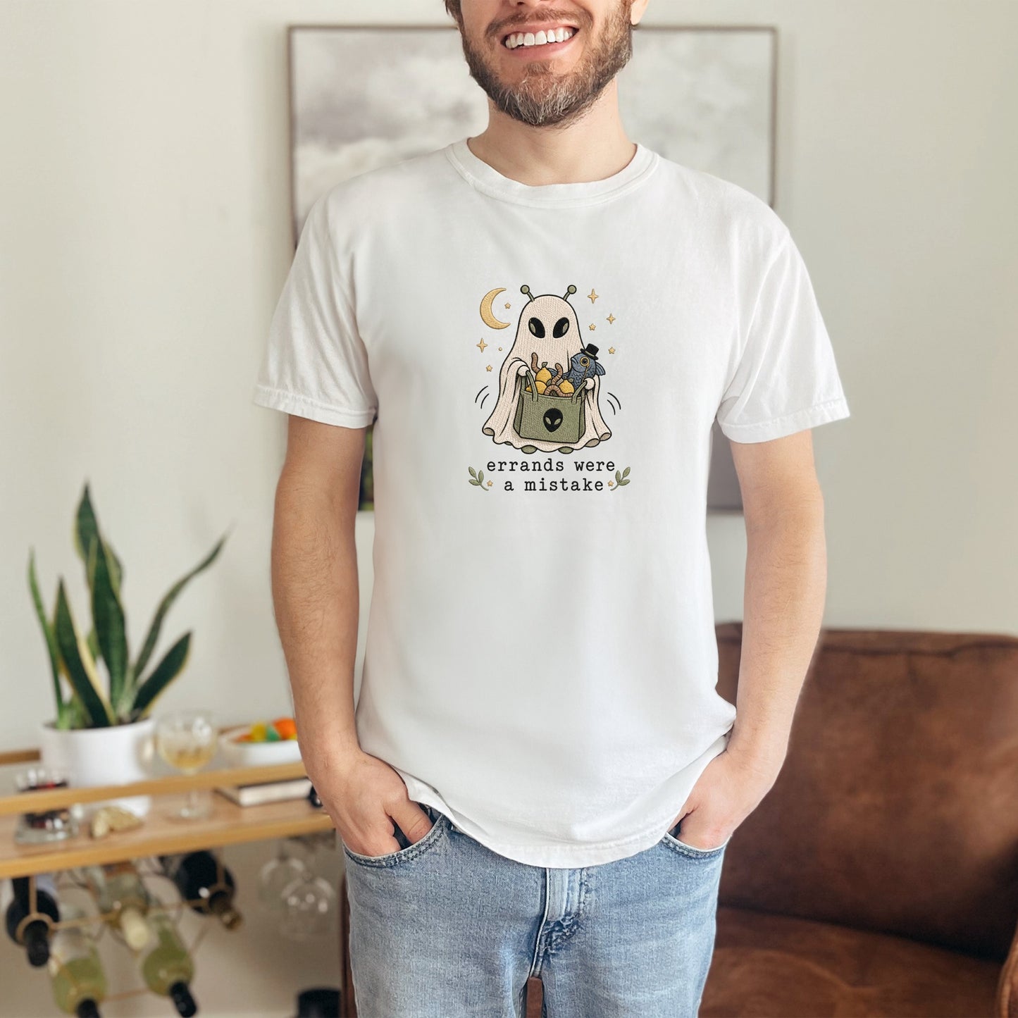 White t-shirt with an alien ghost design holding a basket and text that says "errands were a mistake".