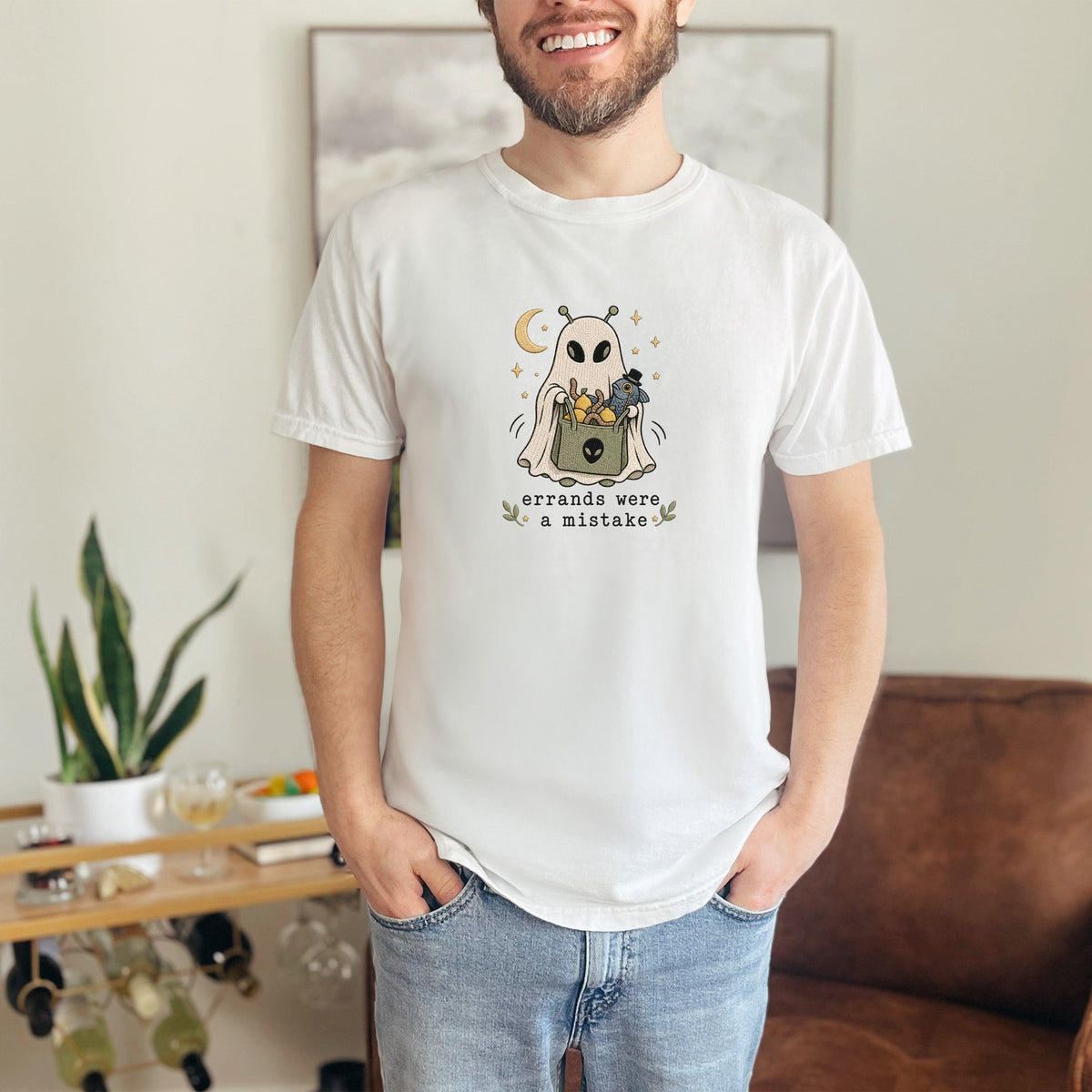 White t-shirt with an alien ghost design holding a basket and text that says "errands were a mistake".