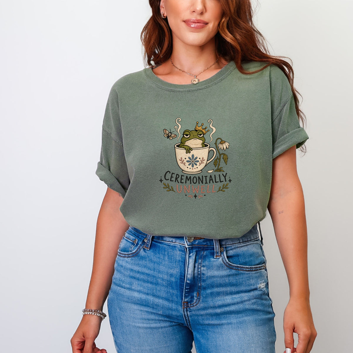 Green t-shirt with graphic of crowned frog in a teacup and text "CEREMONIALLY UNWELL".