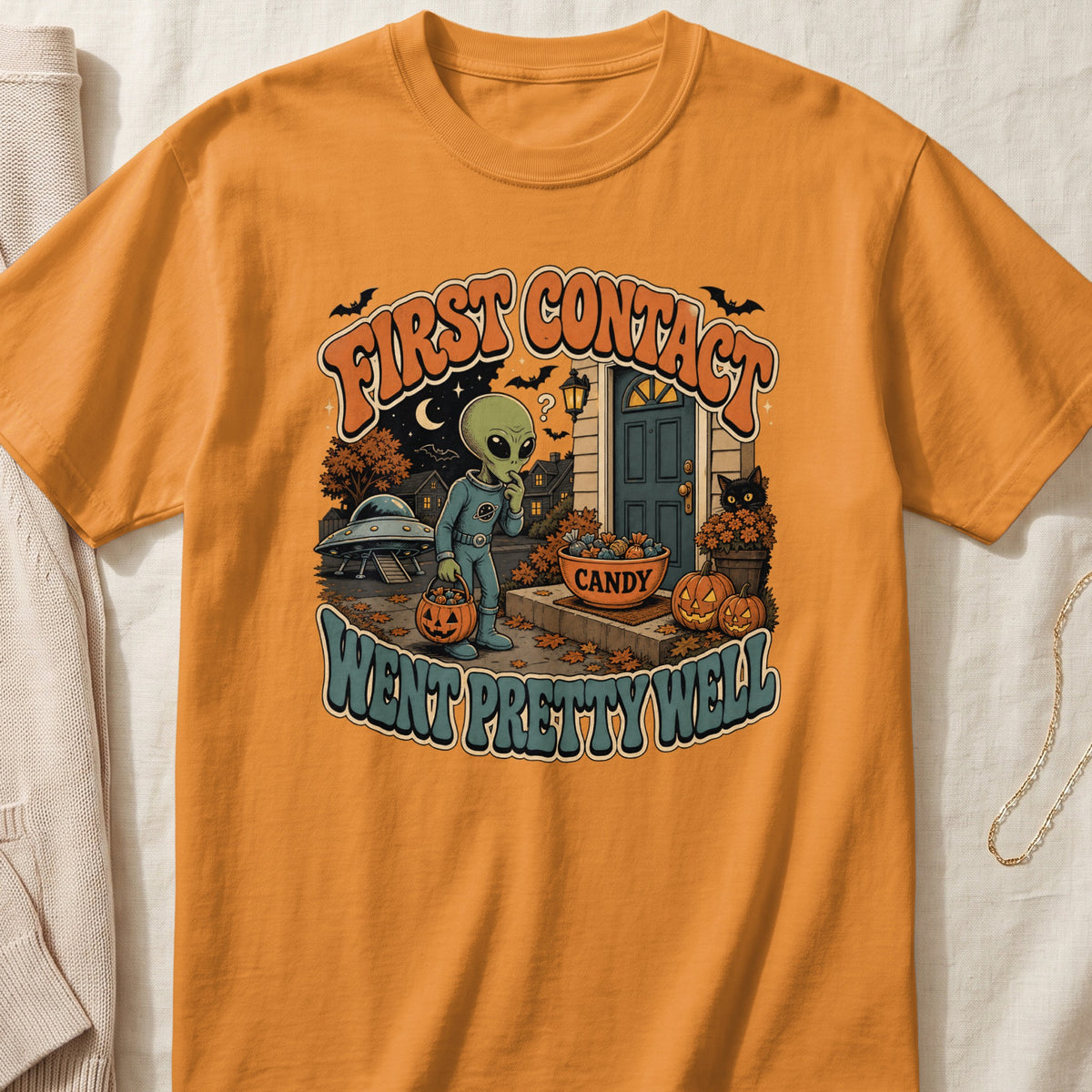 Orange t-shirt with alien trick-or-treating graphic and "First Contact Went Pretty Well" text.