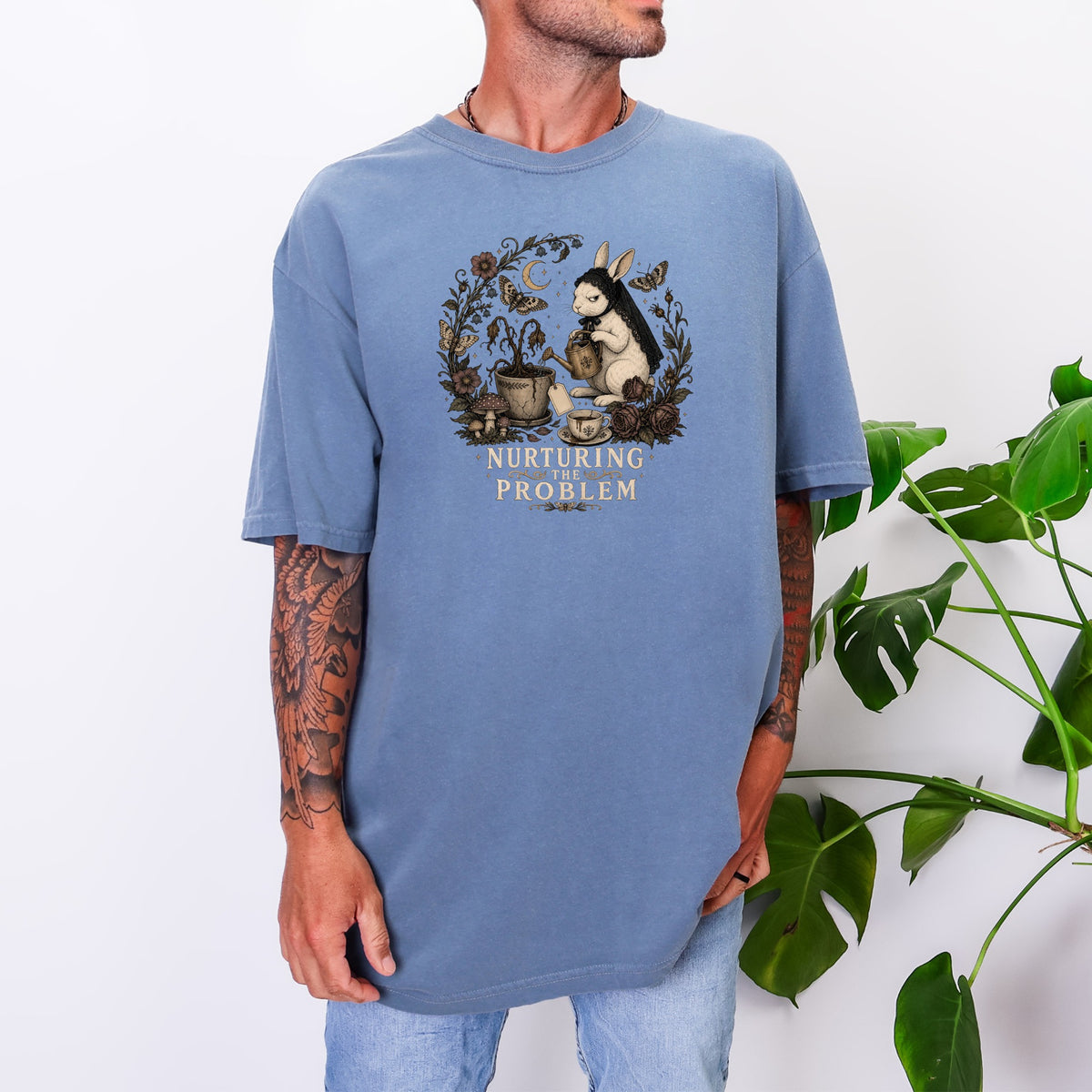 A man wearing an oversized blue t-shirt featuring a vintage rabbit graphic with the text Nurturing the Problem.