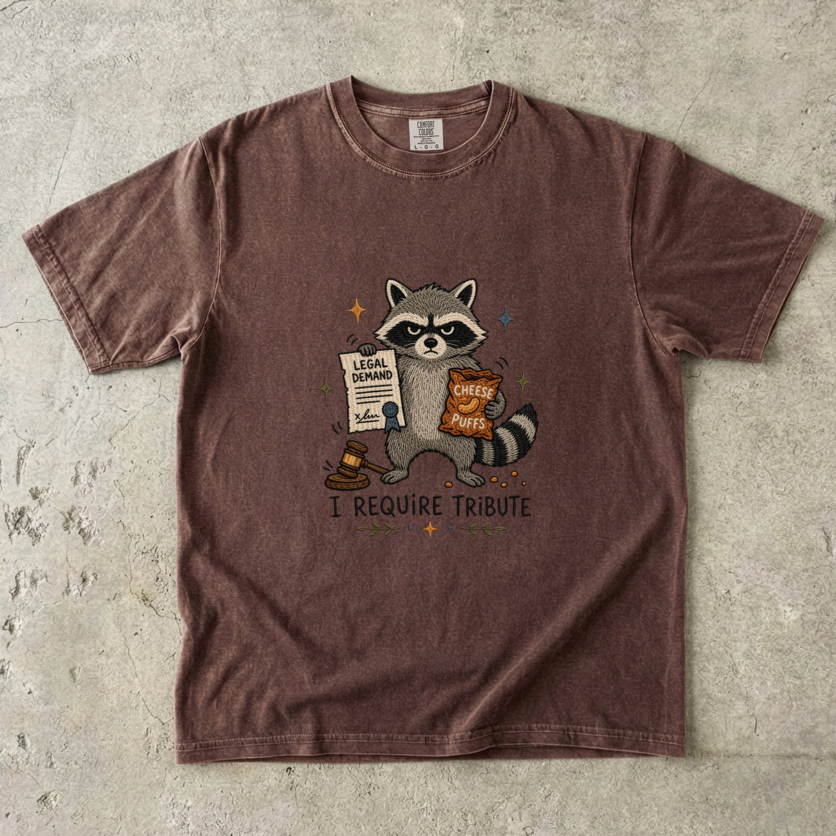Brown t-shirt with raccoon holding legal demand and cheese puffs.