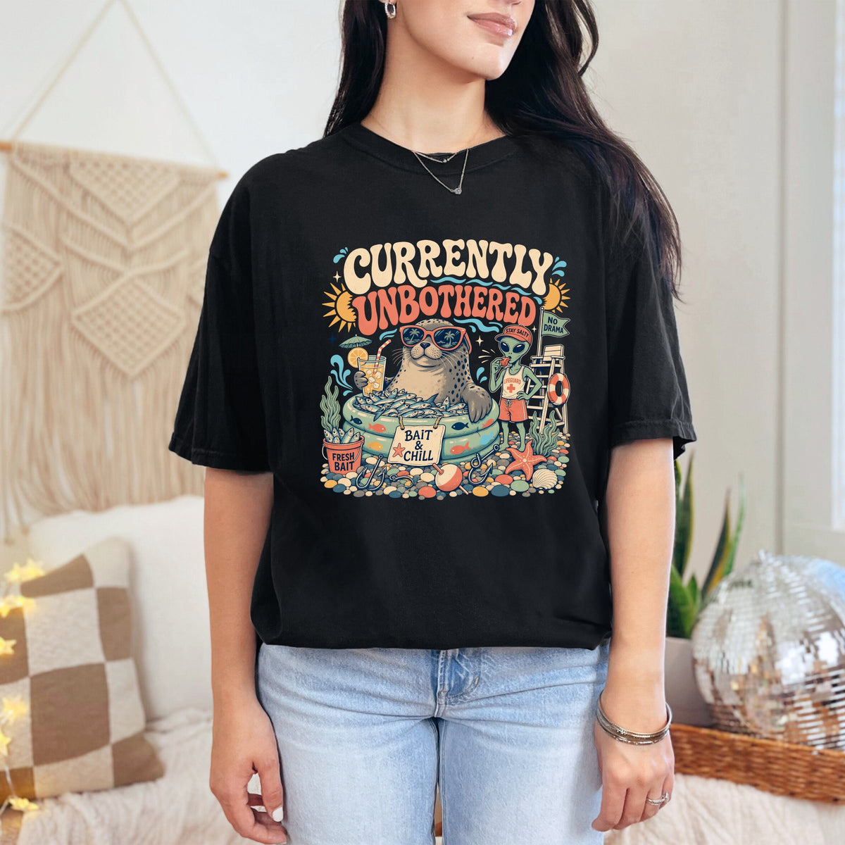 Black t-shirt graphic with seal, alien lifeguard, and text "Currently Unbothered".
