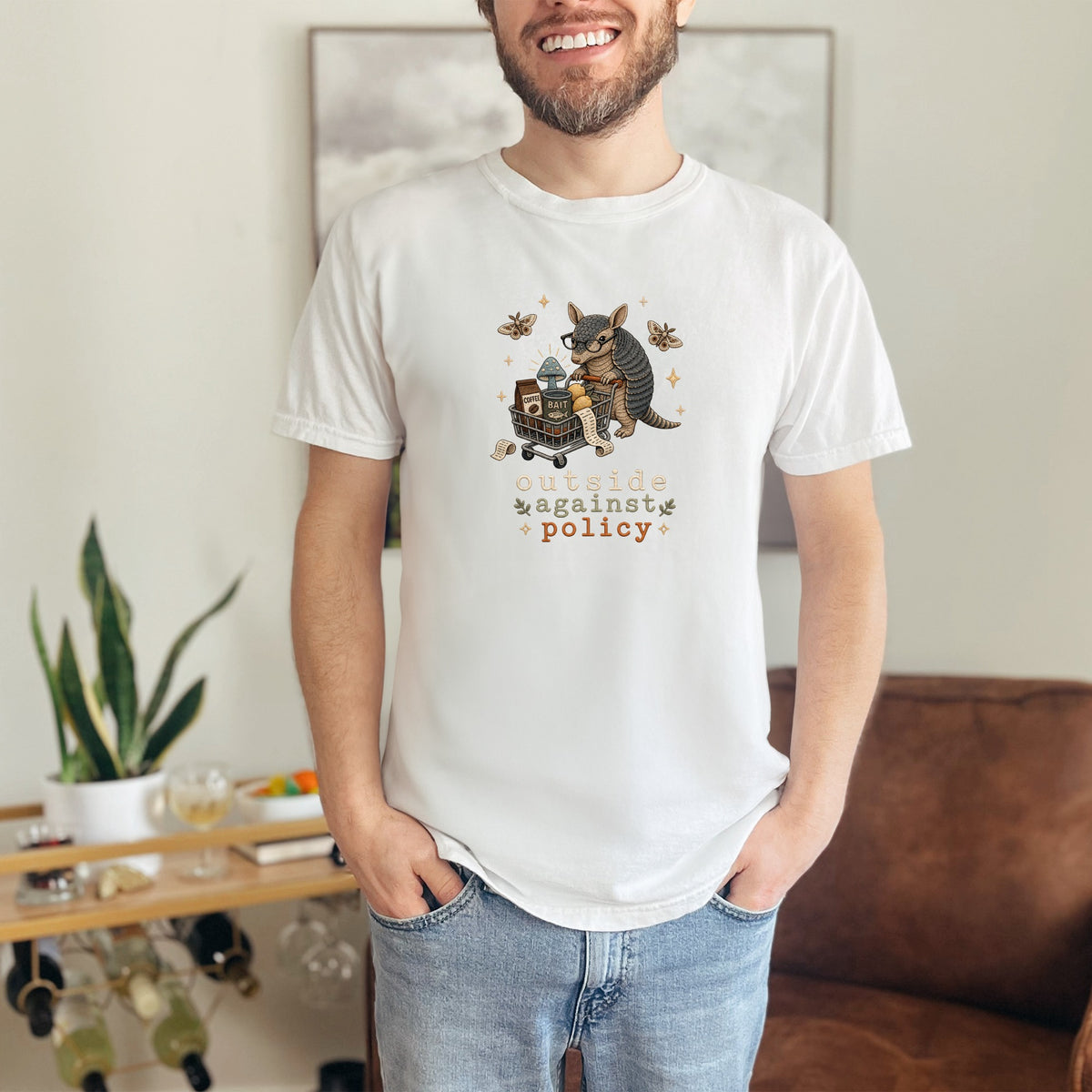 White t-shirt with graphic of armadillo pushing cart, text "outside against policy".
