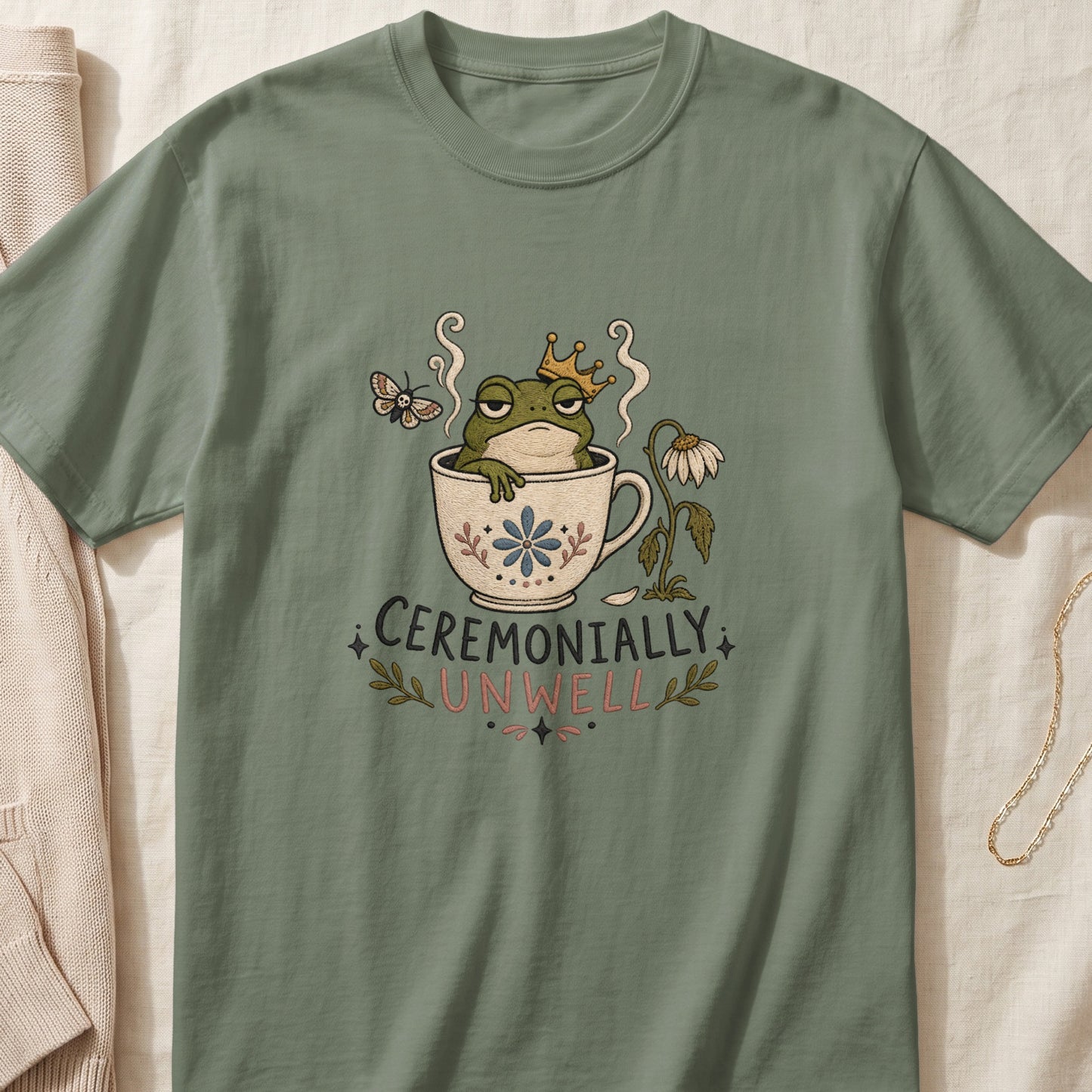 Green t-shirt with a frog wearing a crown in a teacup and text "CEREMONIALLY UNWELL".