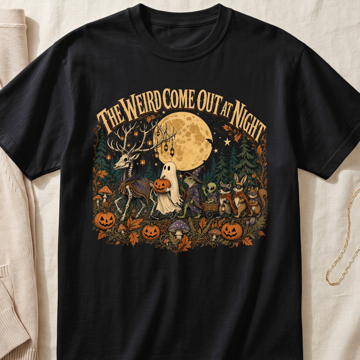 Black t-shirt with "The Weird Come Out at Night" text and Halloween forest scene.