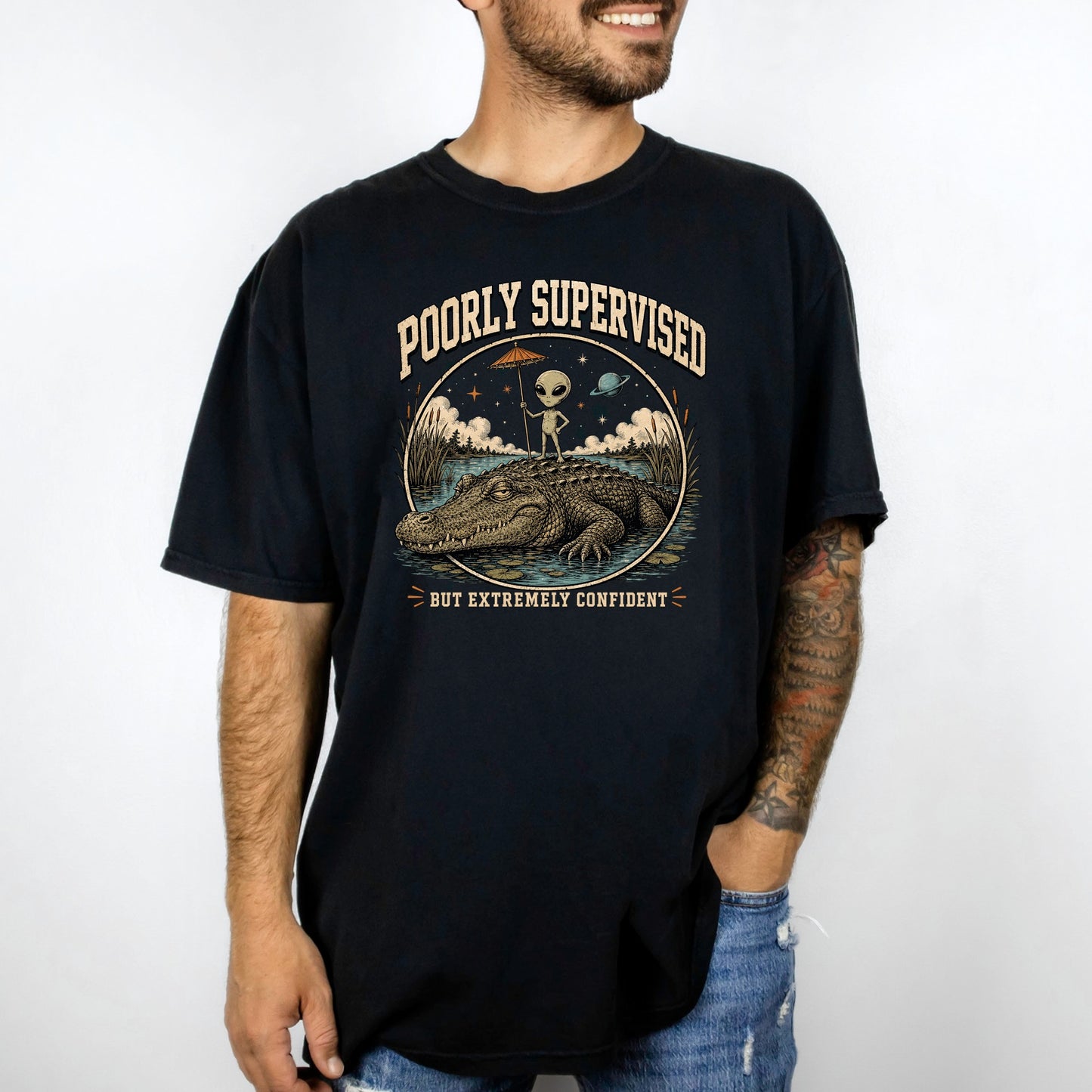 Black t-shirt graphic with an alien on an alligator, text reads "Poorly Supervised but Extremely Confident."