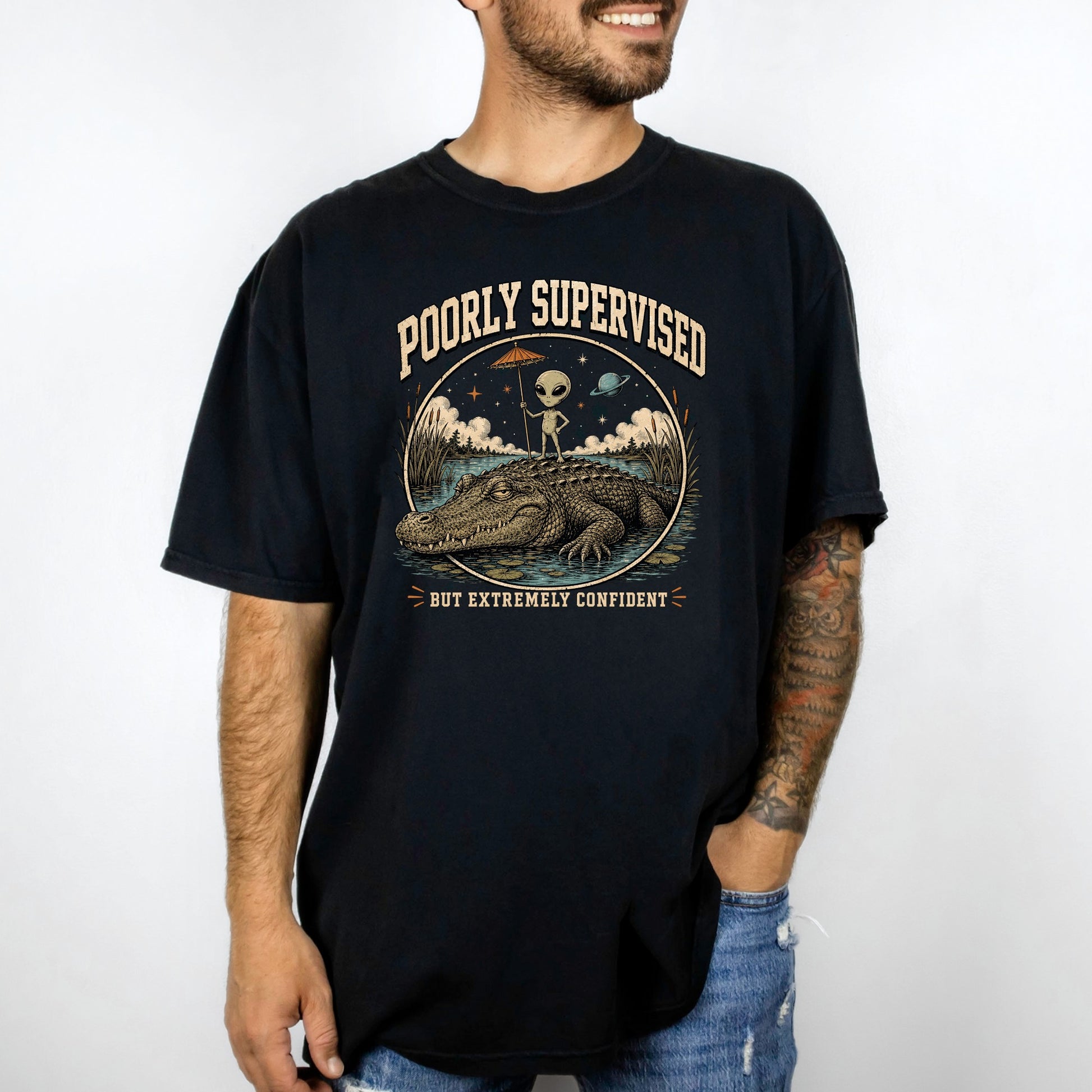 Black t-shirt graphic with an alien on an alligator, text reads "Poorly Supervised but Extremely Confident."