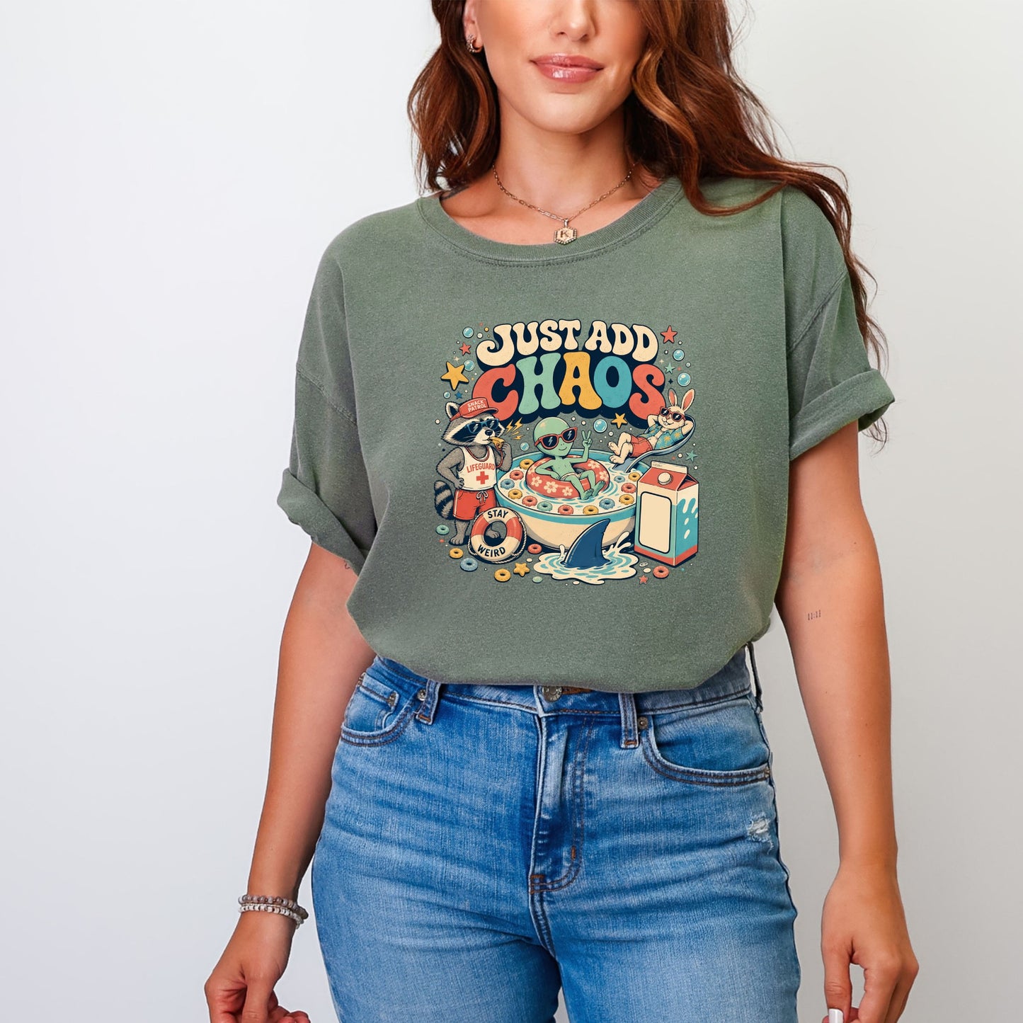 A woman wearing an olive green t-shirt with a colorful retro graphic and blue jeans.