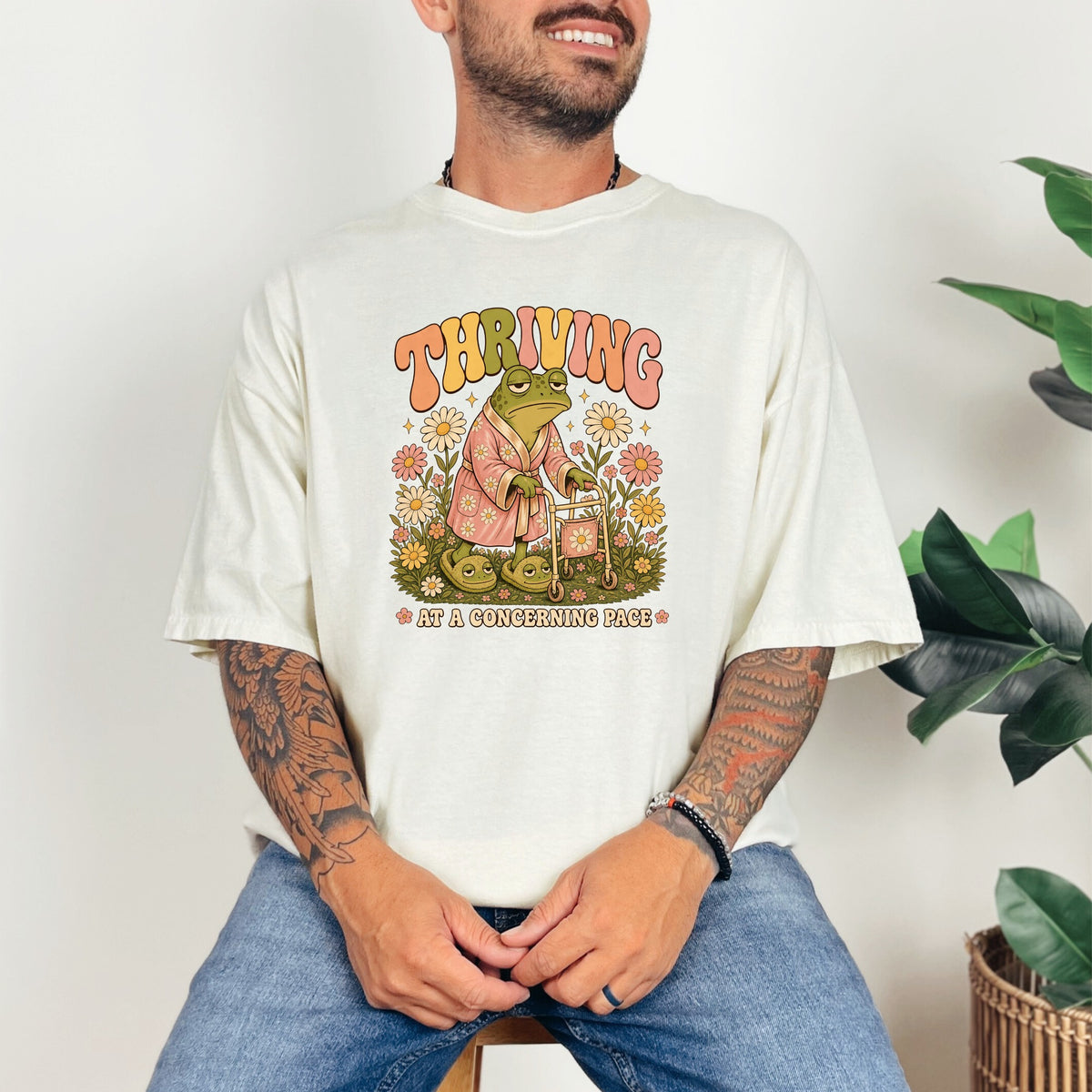 Graphic of a frog in a robe with a walker and flowers, text says "THRIVING AT A CONCERNING PACE".