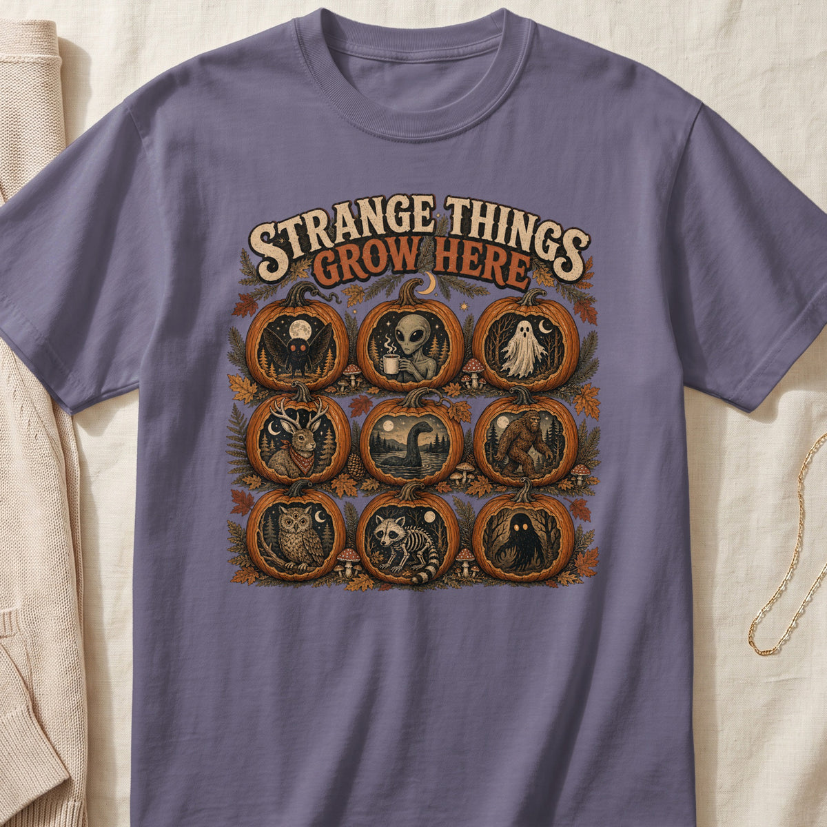 Shirt with "Strange Things Grow Here" text and nine pumpkins featuring cryptids and Halloween figures.