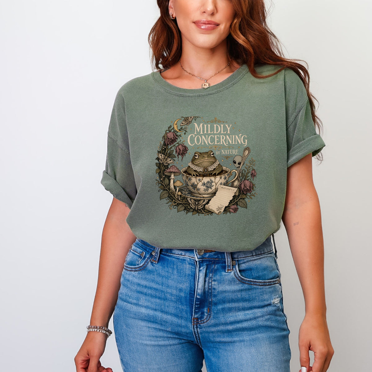 T-shirt graphic with a frog in a teacup, mushrooms, and "MILDLY CONCERNING BY NATURE" text.