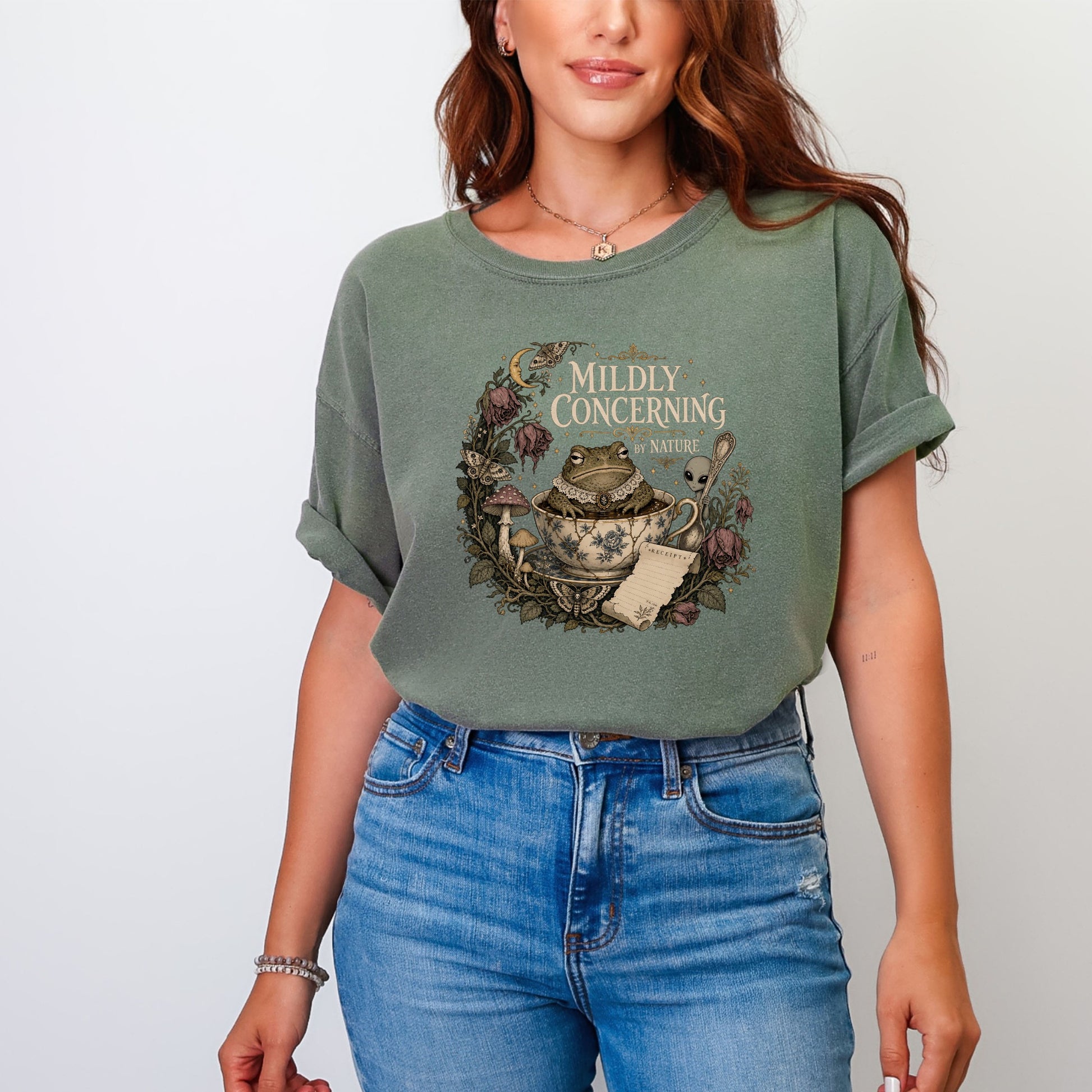 T-shirt graphic with a frog in a teacup, mushrooms, and "MILDLY CONCERNING BY NATURE" text.