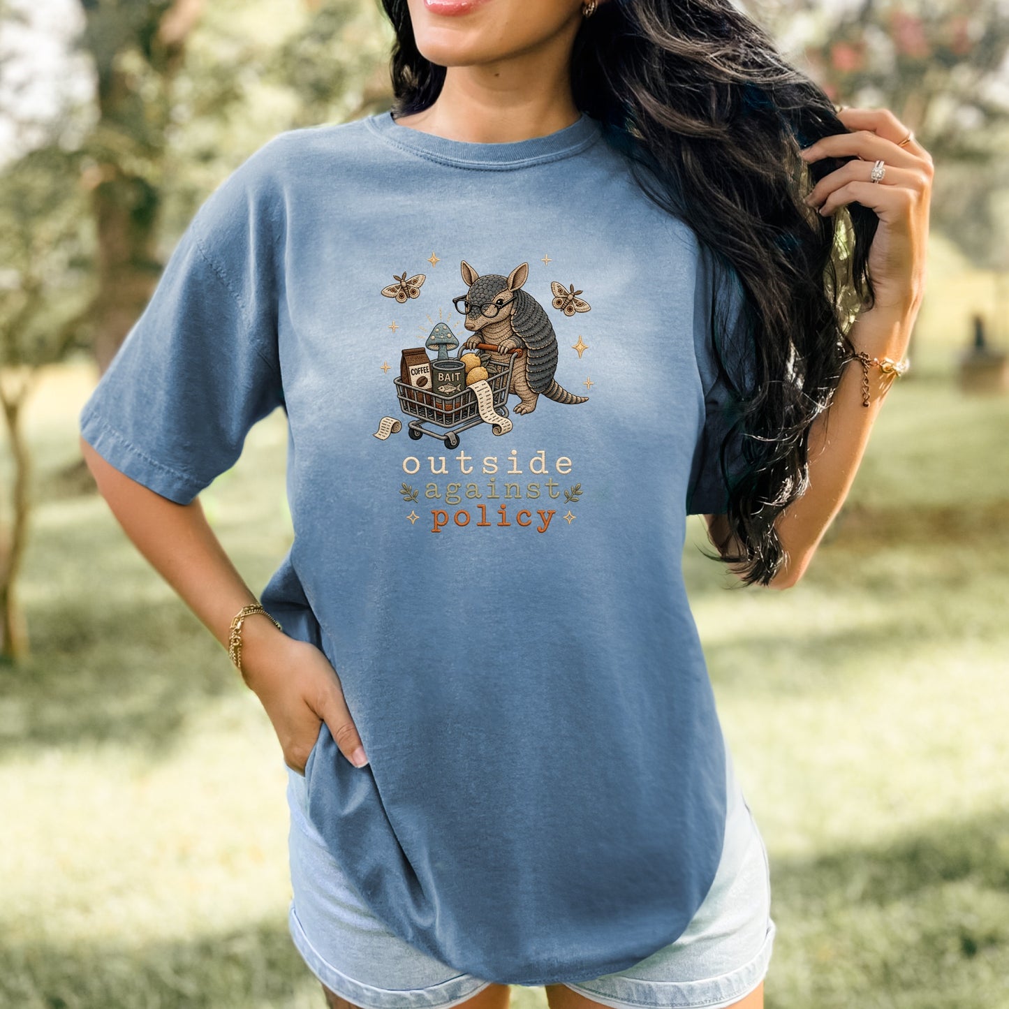 Blue t-shirt with armadillo pushing a shopping cart, reading "outside against policy".