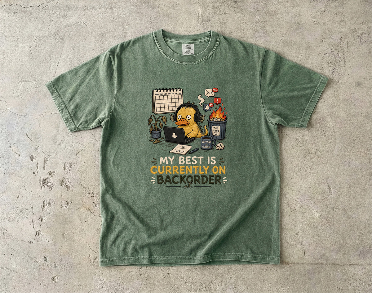 Green t-shirt with cartoon duck at computer, text "MY BEST IS CURRENTLY ON BACKORDER".