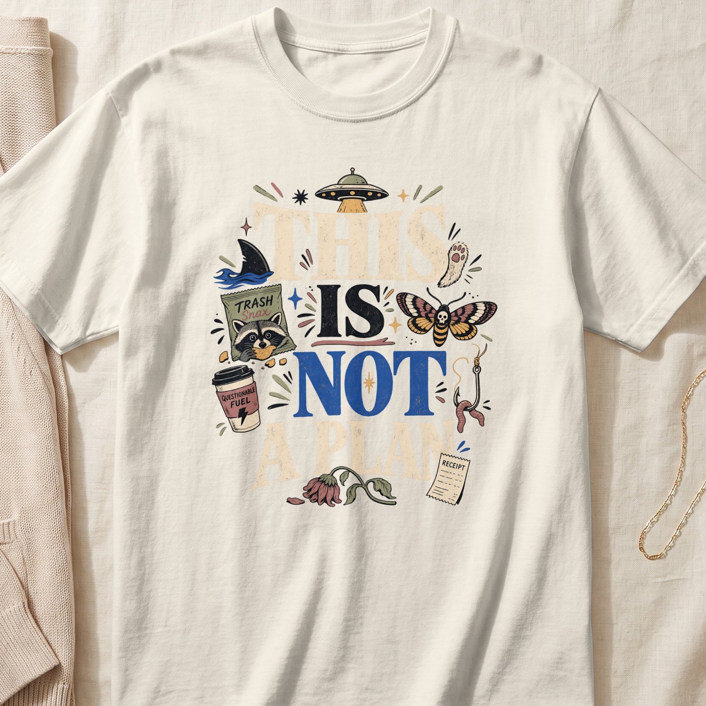 Cream t-shirt with "THIS IS NOT A PLAN" text and quirky illustrations.