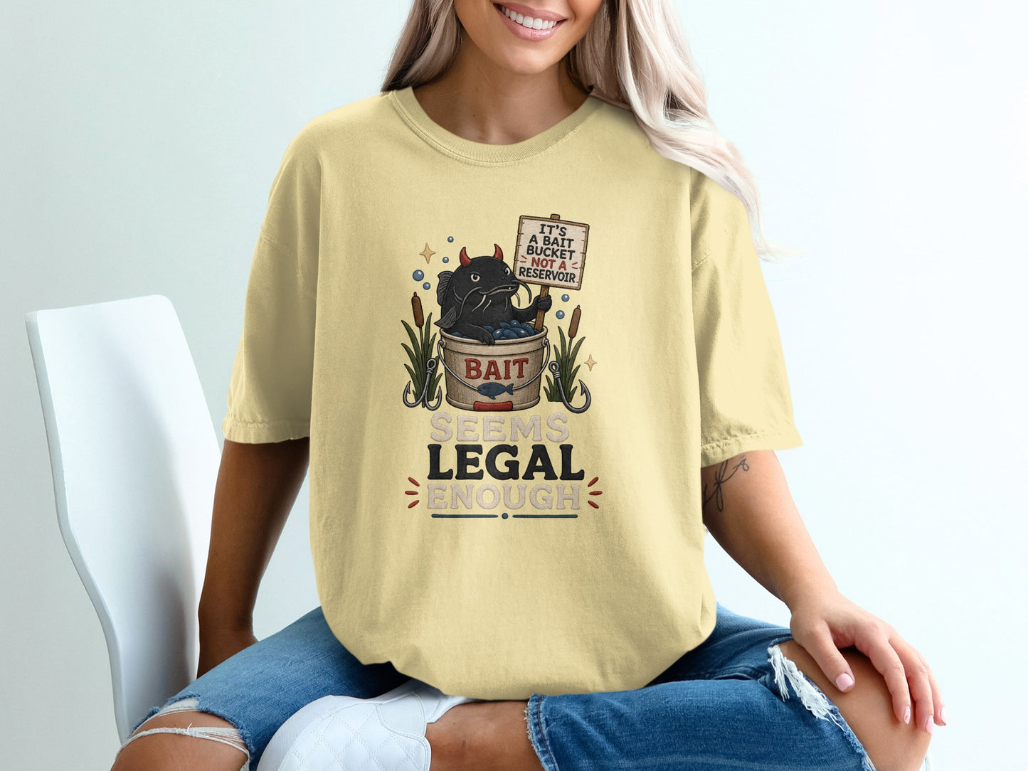 Yellow t-shirt graphic with devil cat holding sign: "It's a bait bucket not a reservoir."