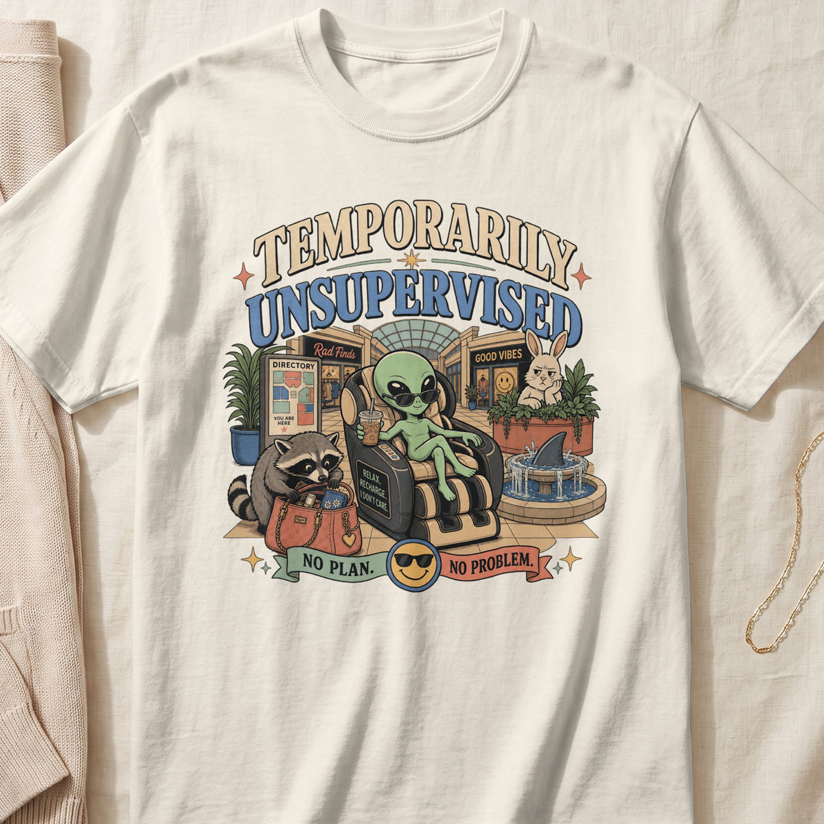 Off-white t-shirt featuring a cartoon graphic of an alien relaxing in a massage chair at a mall, surrounded by animals and the text "TEMPORARILY UNSUPERVISED, NO PLAN. NO PROBLEM."