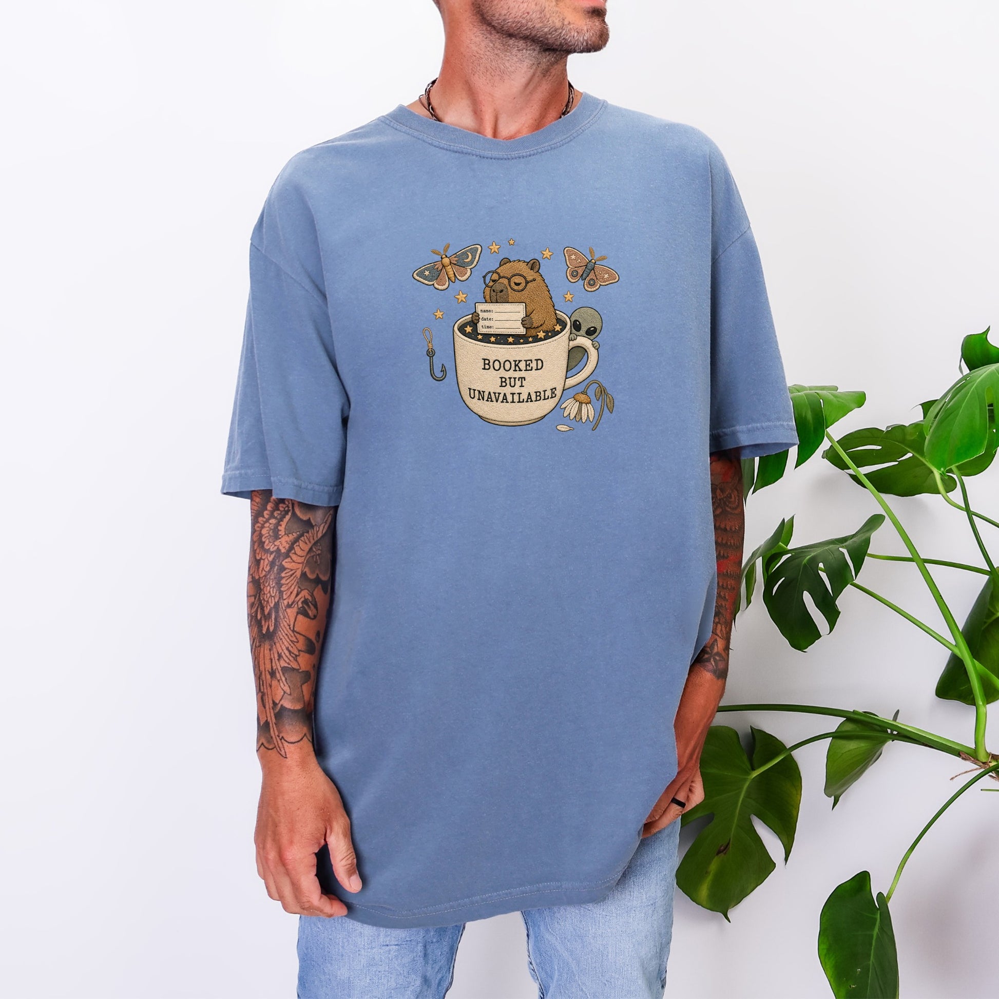 Blue t-shirt with graphic of a bear in a mug that reads "BOOKED BUT UNAVAILABLE".
