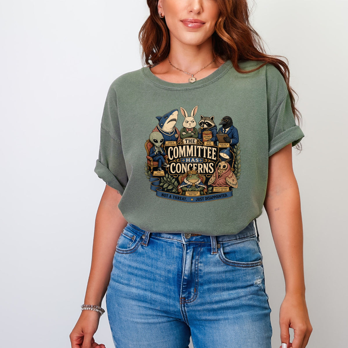 A person wearing an olive green t-shirt featuring a graphic of anthropomorphic animals and text reading The Committee Has Concerns.