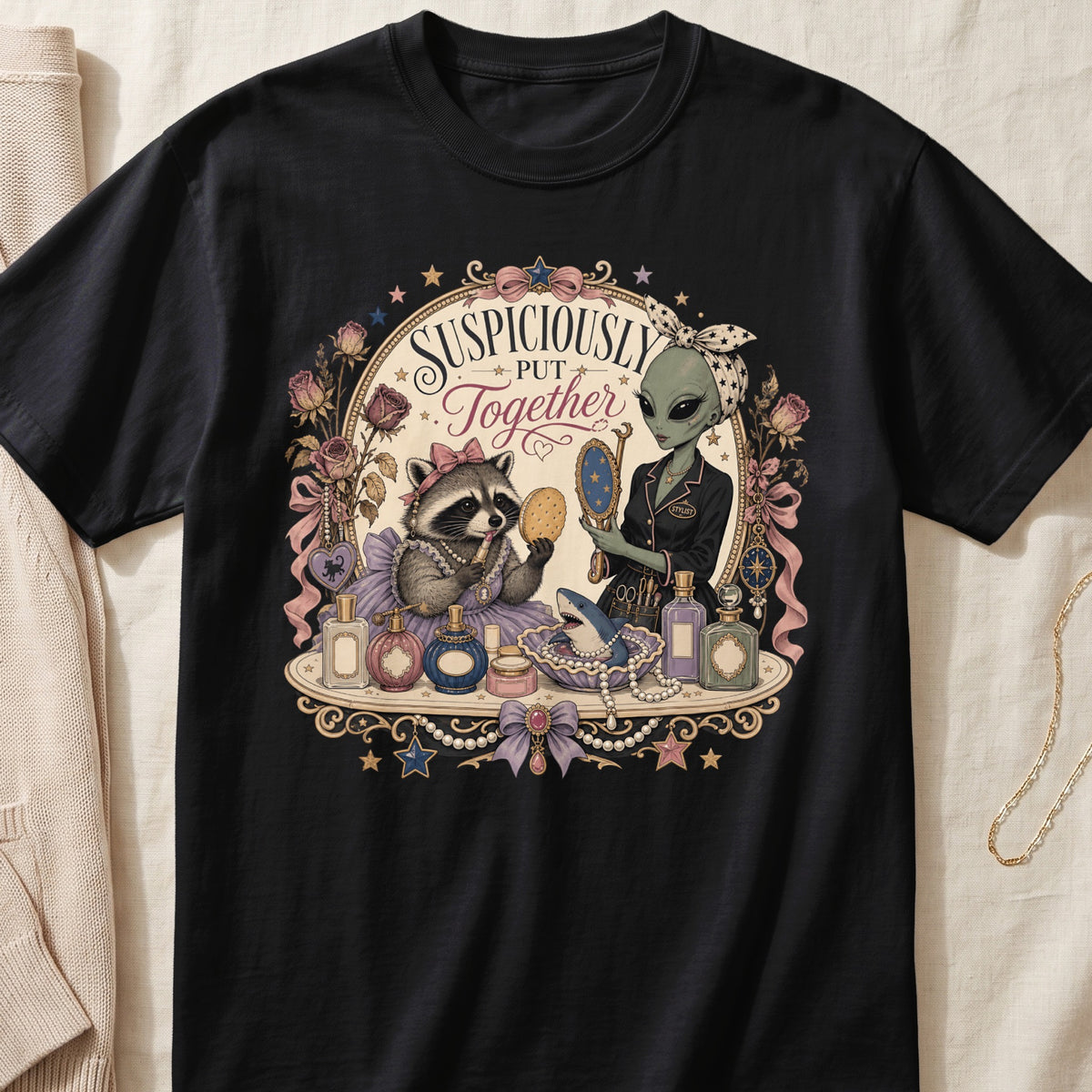 Black t-shirt featuring an ornate graphic of an alien and a raccoon holding cosmetics, with the text Suspiciously Put Together.