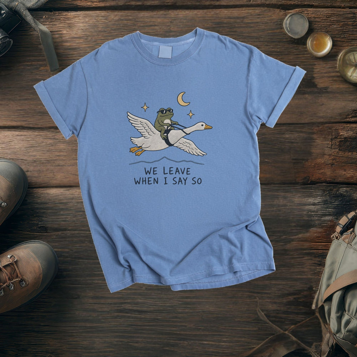 Blue t-shirt with graphic of frog riding a goose under the moon and stars.