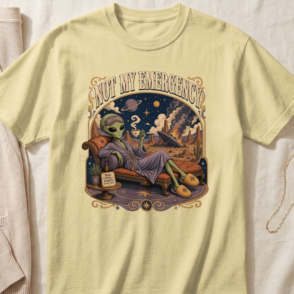 Yellow t-shirt with an alien relaxing, "Not My Emergency" text, and space scene.