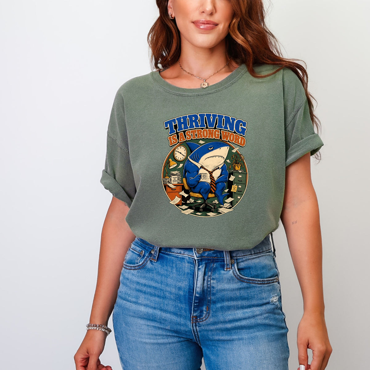 Green t-shirt with a graphic of a shark in a suit saying "Thriving is a strong word".