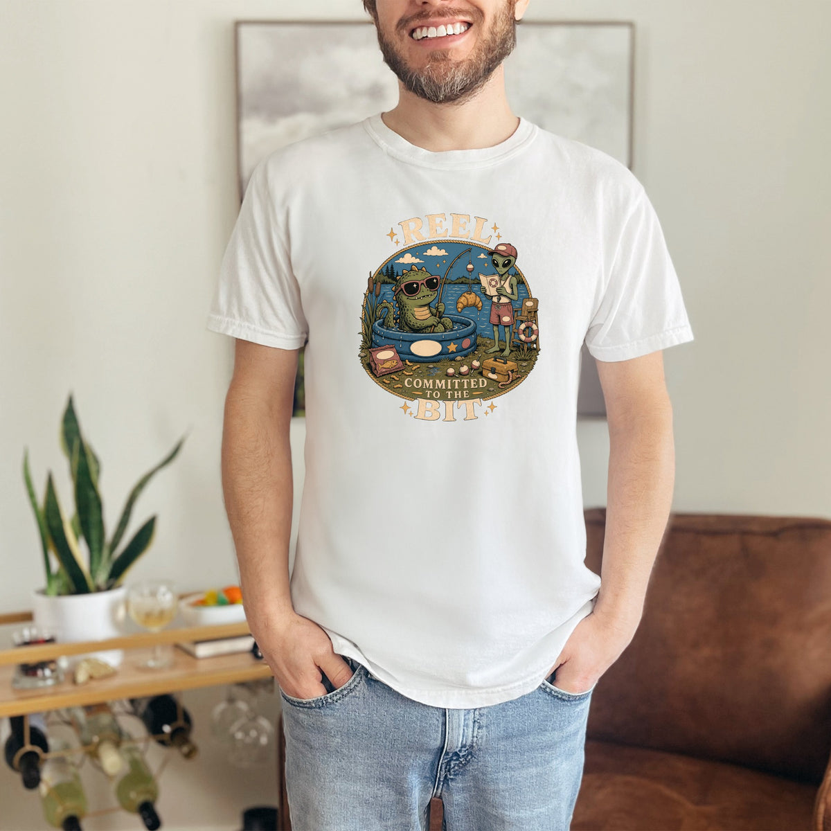 T-shirt with graphic of a dinosaur and alien fishing, text "Reel Committed to the Bit".