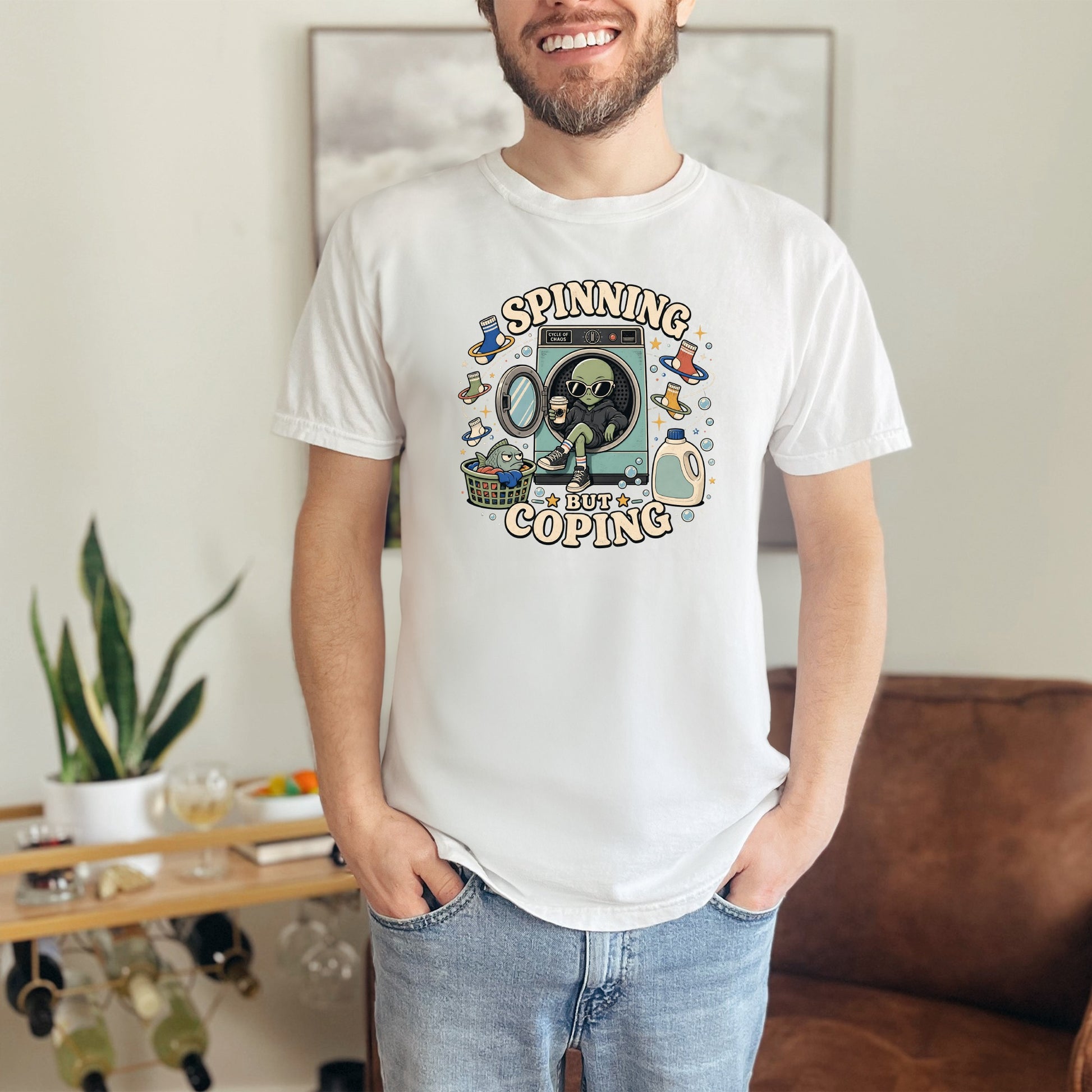 White t-shirt graphic of an alien in a dryer with text "SPINNING BUT COPING".