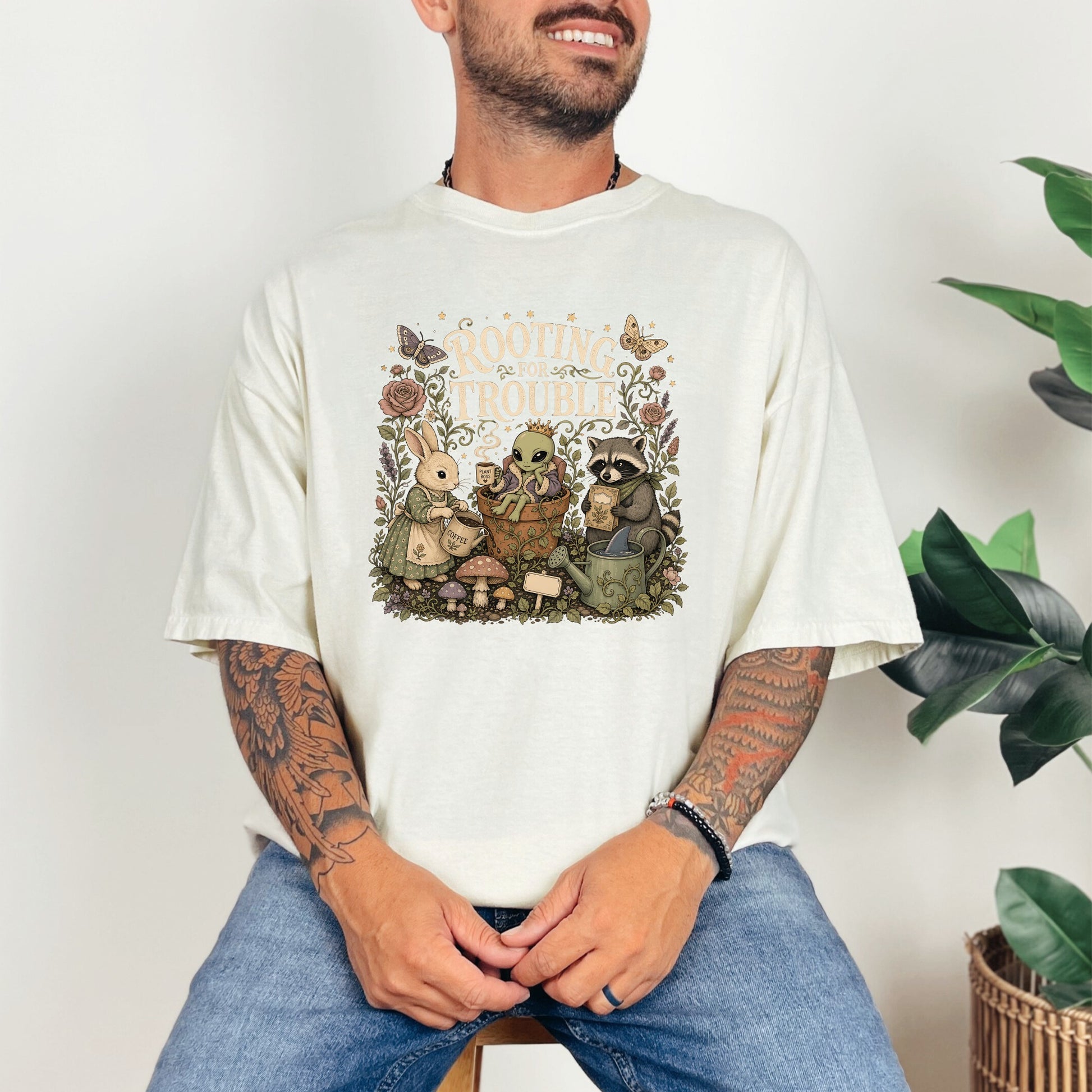 T-shirt graphic with bunny, alien, and raccoon characters around plants and mushrooms.