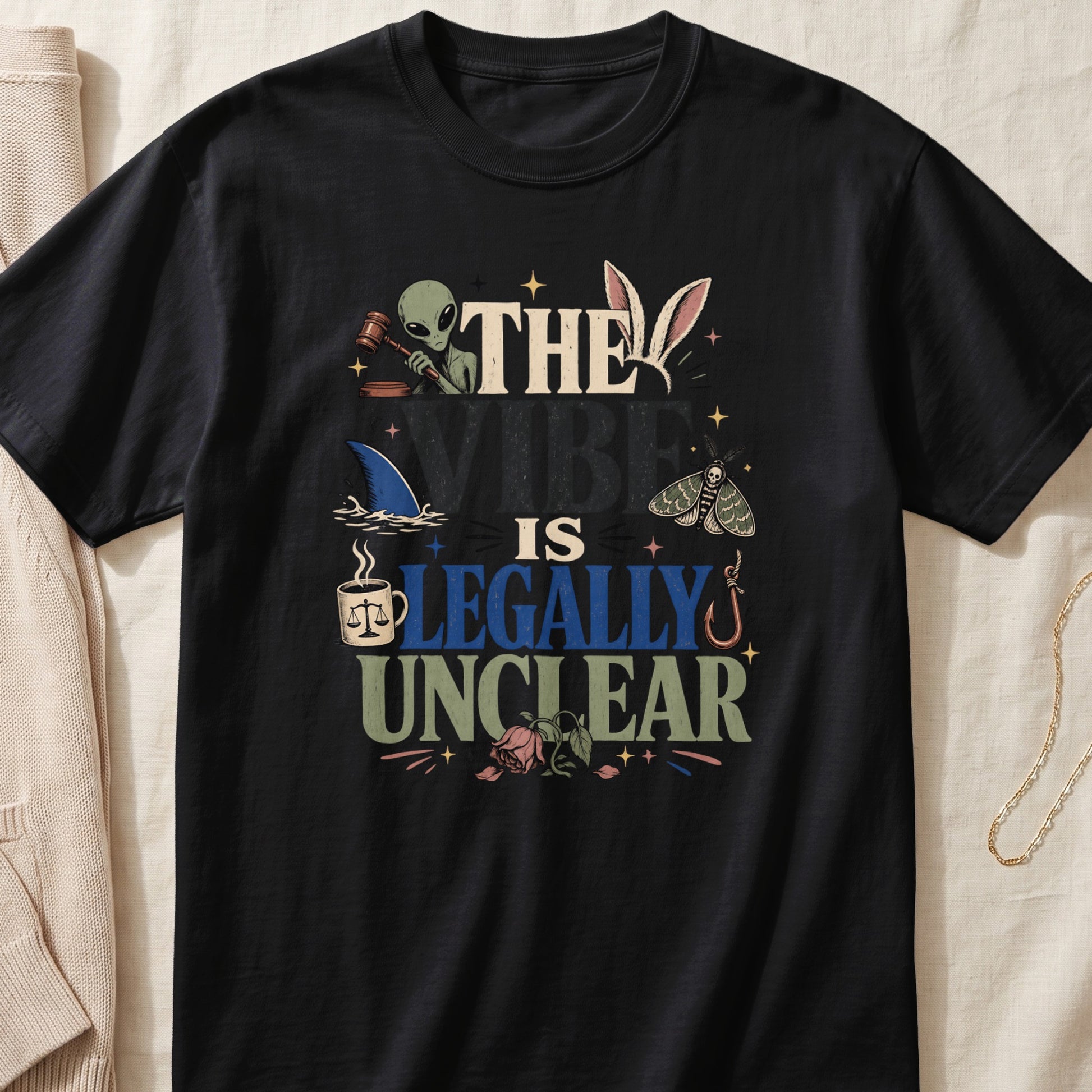 Black t-shirt with text "The Vibe Is Legally Unclear" and various illustrations.