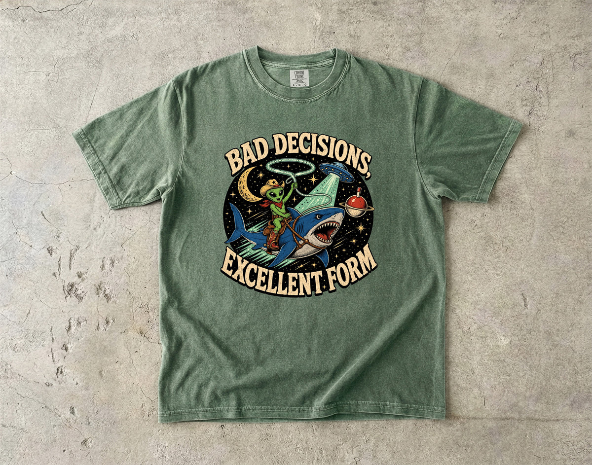 Green t-shirt with alien riding shark, UFO, moon, stars, and text "BAD DECISIONS, EXCELLENT FORM".