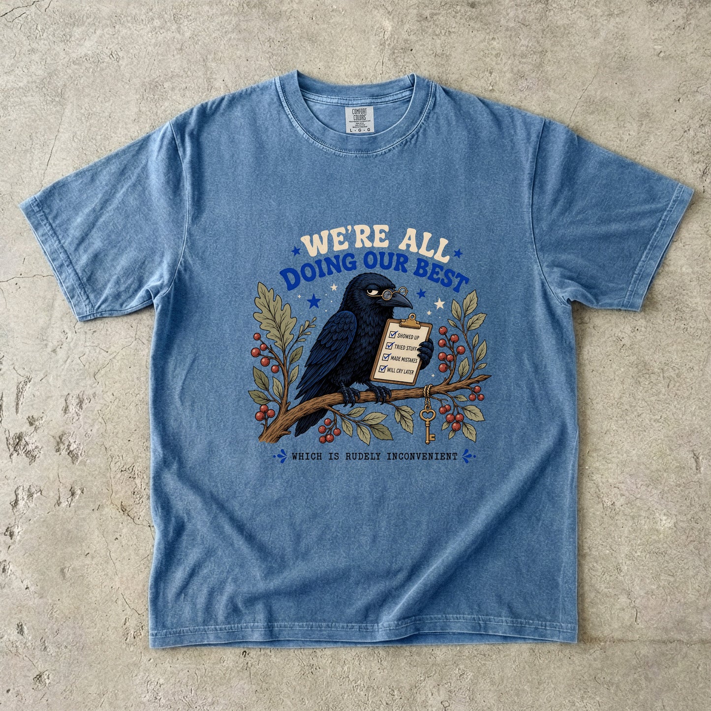 Blue t-shirt with crow wearing glasses holding a checklist, text says "We're All Doing Our Best Which Is Rudely Inconvenient".