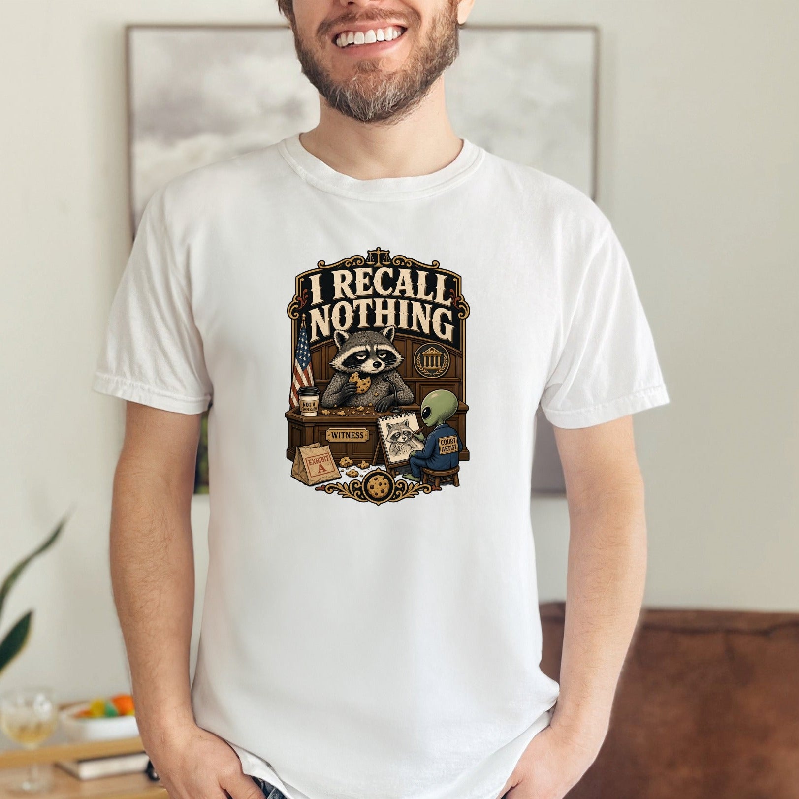 T-shirt graphic: Raccoon witness eating cookies, alien artist, and text "I Recall Nothing."