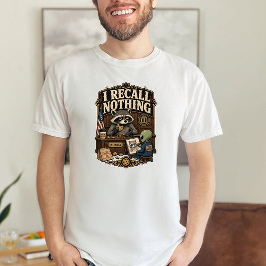T-shirt graphic: Raccoon witness eating cookies, alien artist, and text "I Recall Nothing."