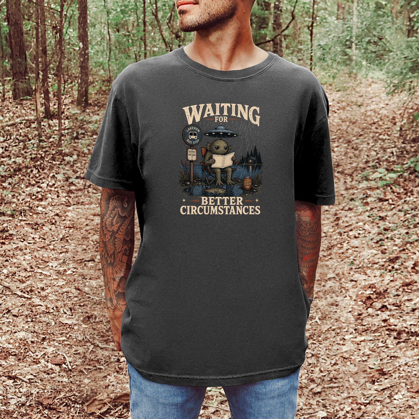 T-shirt graphic of a creature at a bus stop with UFO and text "Waiting for Better Circumstances."